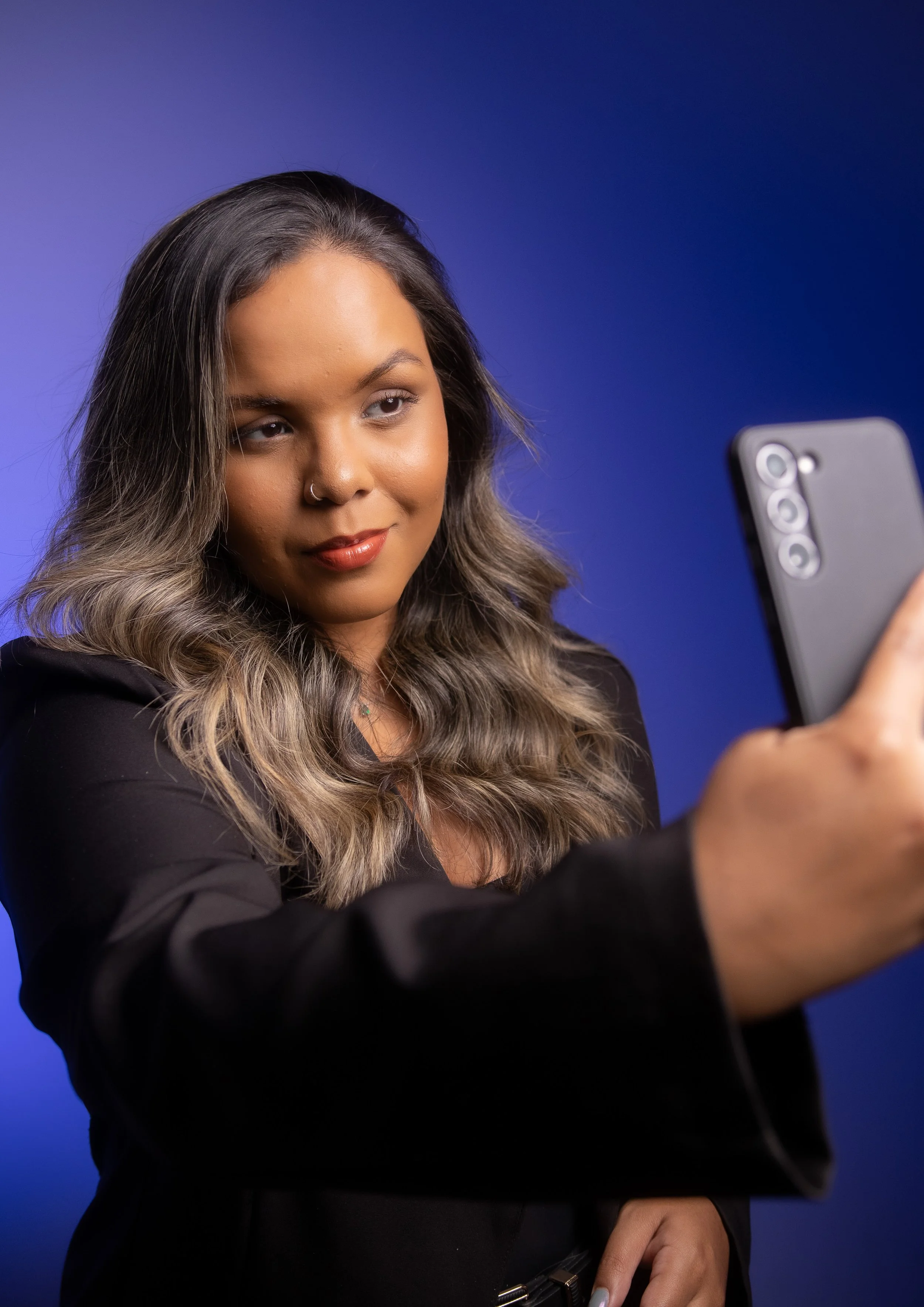 Mulher com cabelo castanho e ondulado segurando um smartphone para tirar uma selfie, fundo azul