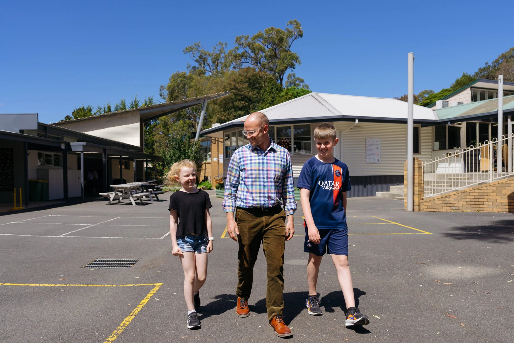 Male teacher walks across courtyard with a student on each side of him