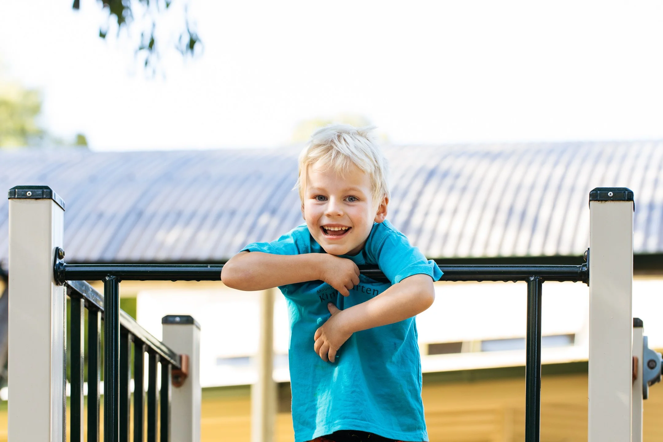 Young male student holds onto playground railing and smiles at camera