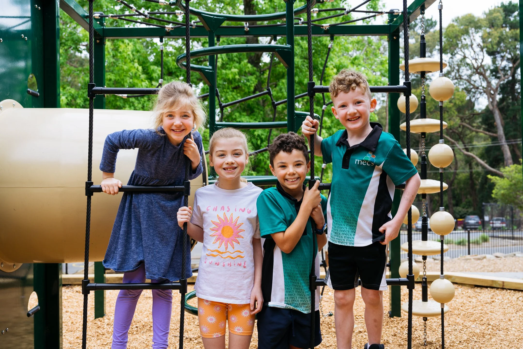 4 Primary aged students utilise play equipment and are facing the camera, smiling