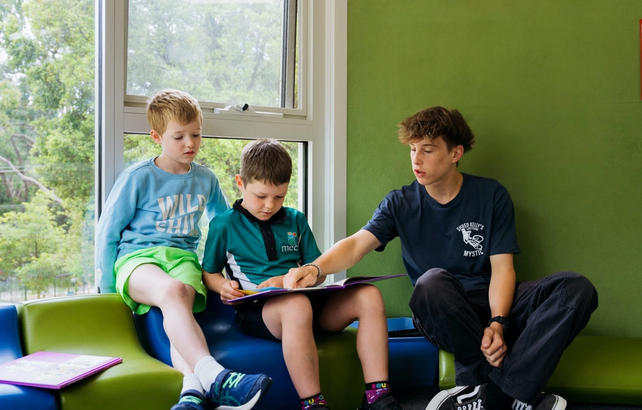 Two young male students seated with a senior male student. They are in a classroom reading a picture book.