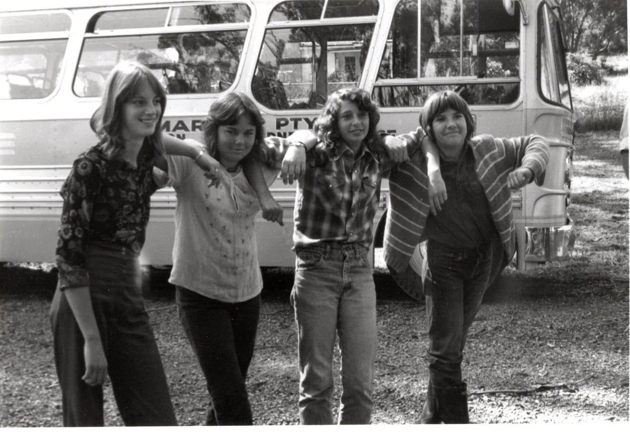 Vintage black and white photograph of four students standing casually in front of of the school bus