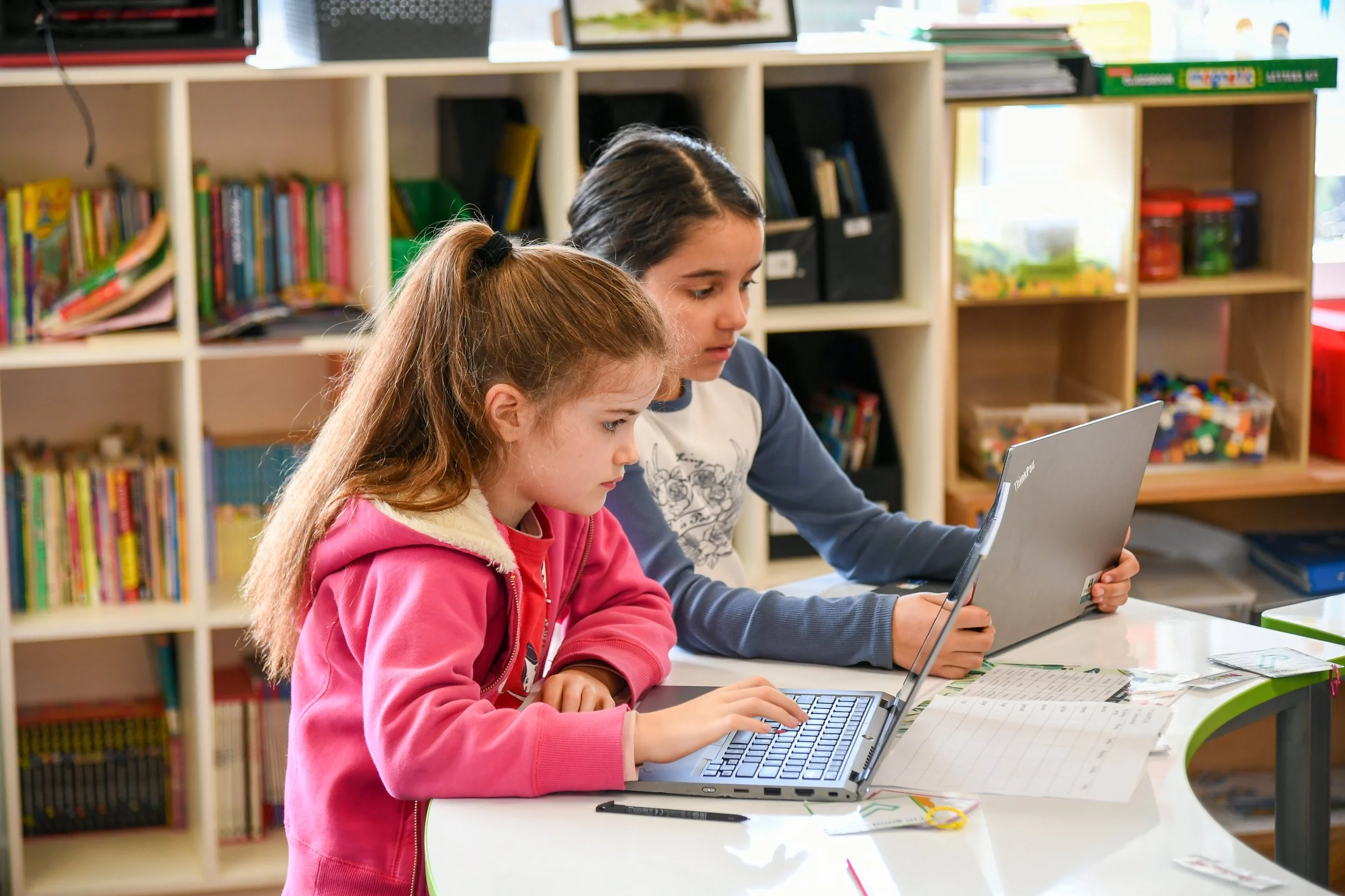 Side profile of two Primary aged girls working at laptops in a classroom