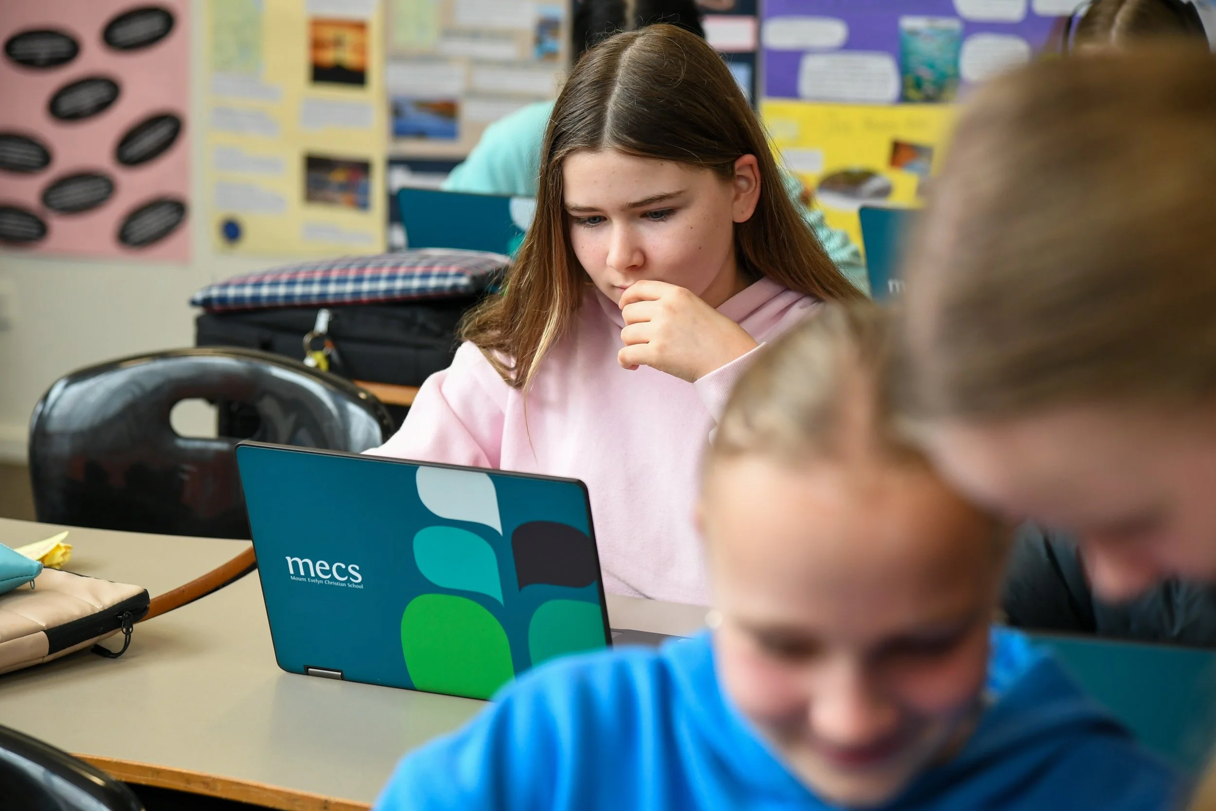 Female teenage student seated in classroom looking at laptop