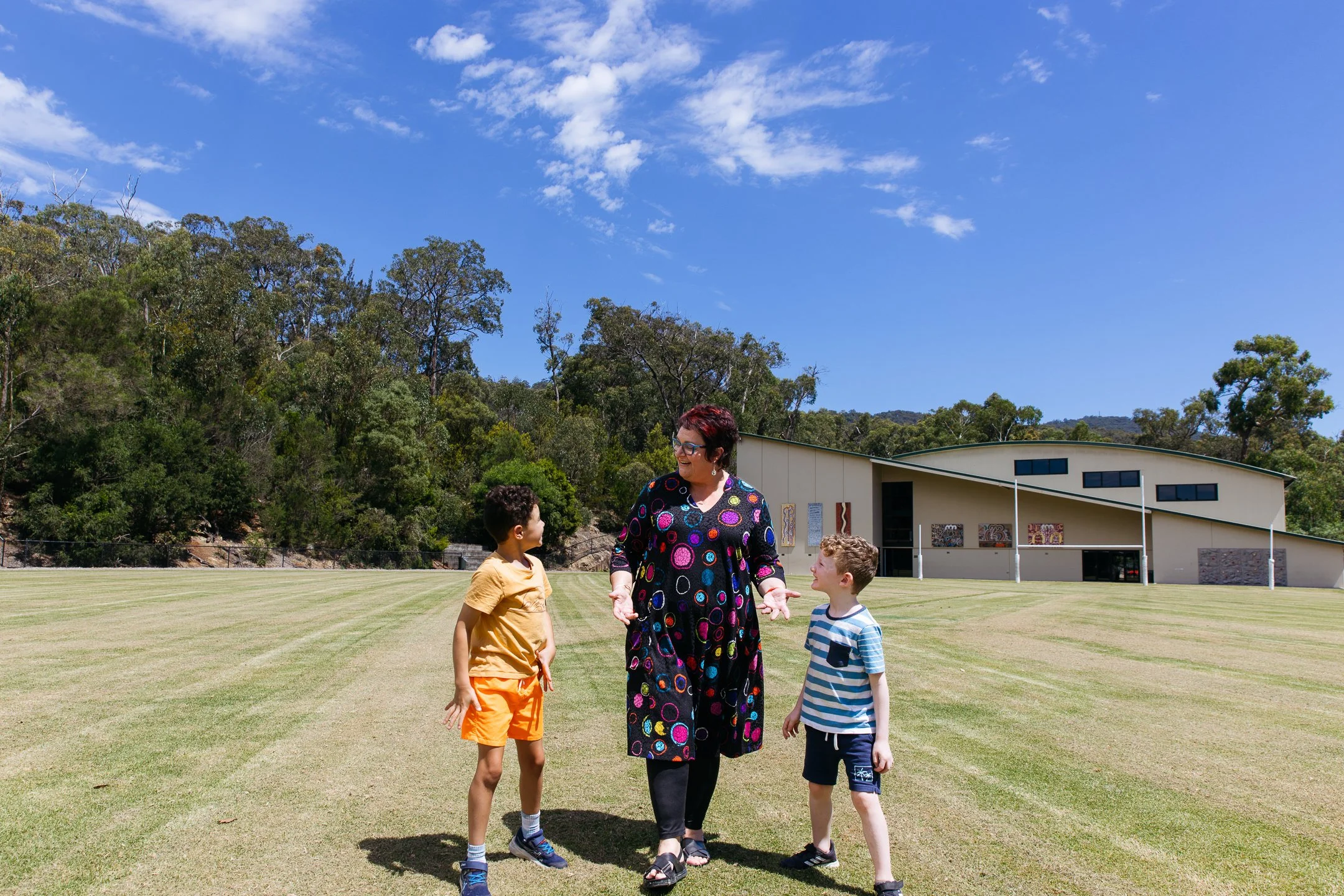 Female adult walking across oval with two Primary school aged boys on either side of her