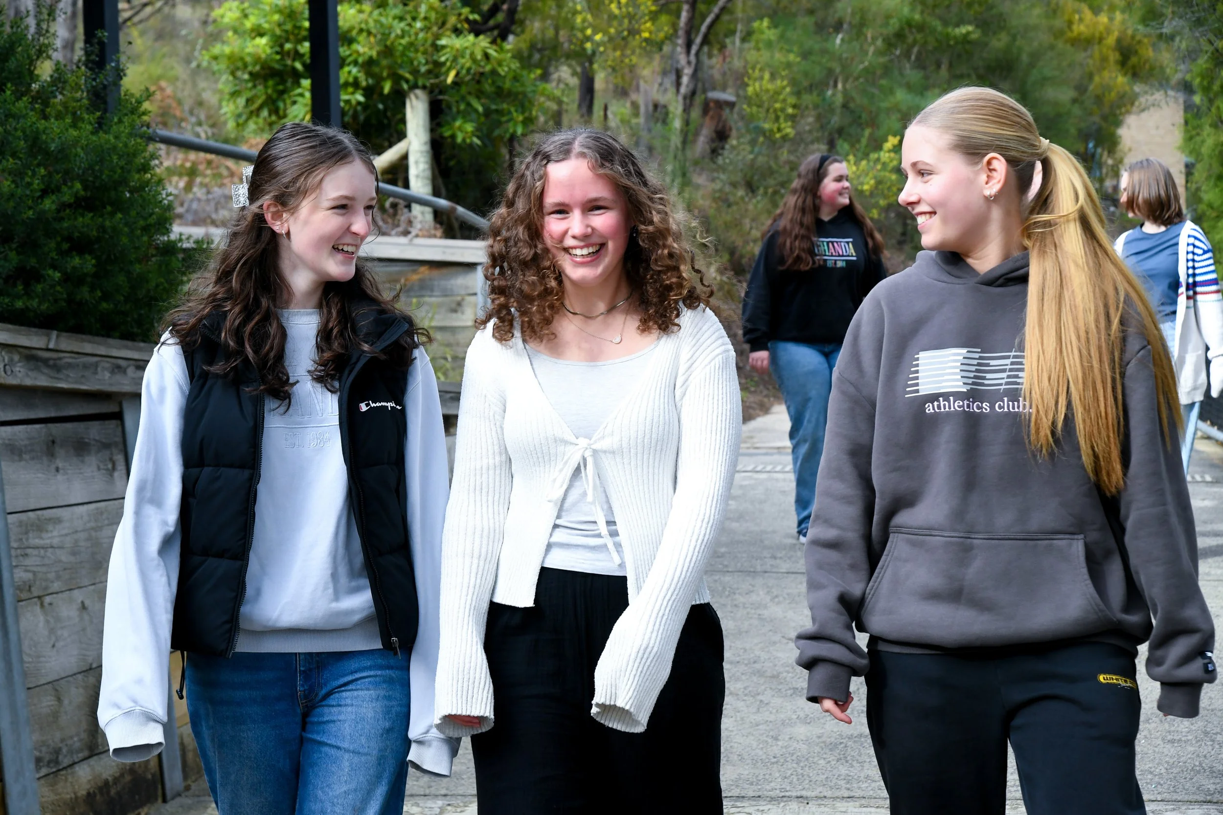 Three senior girls walking down pathway, candidly talking and laughing.