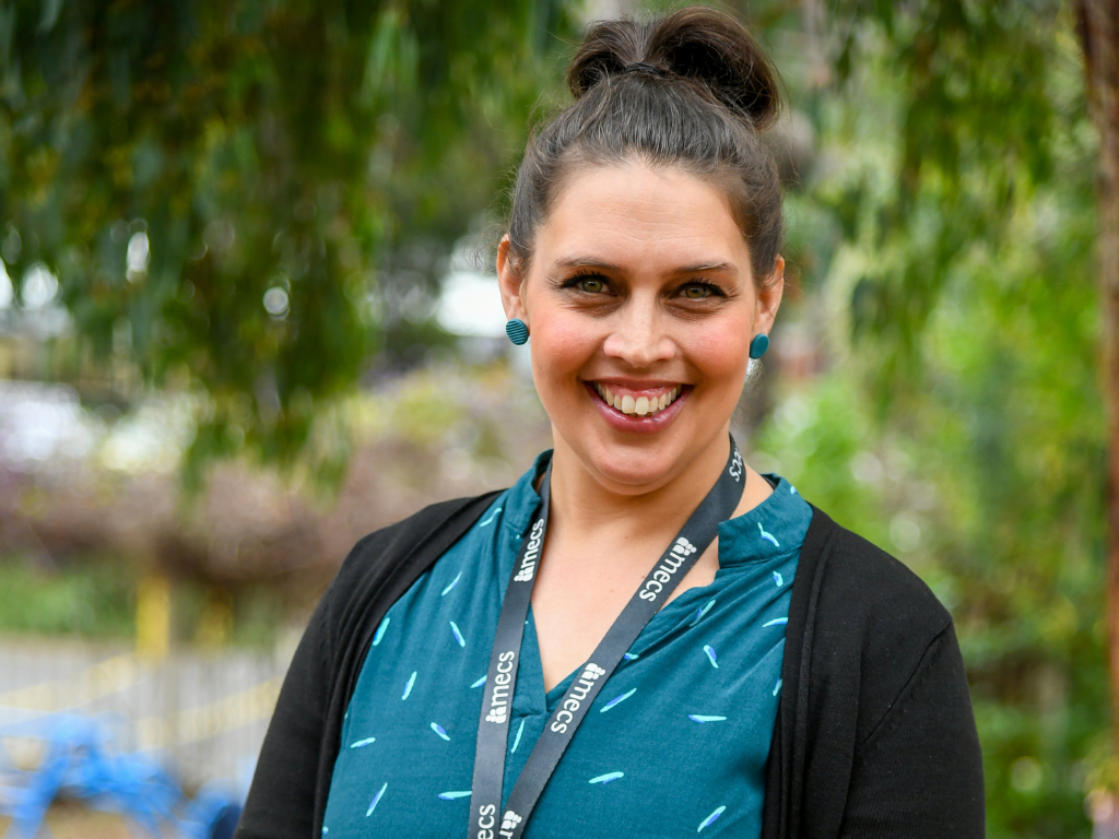 Adult female wearing dark green top, black cardigan and MECS lanyard smiles at camera.