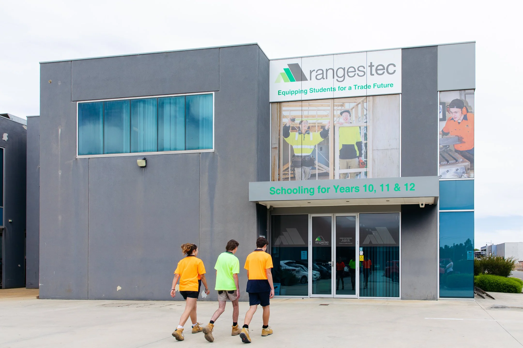 Three students in hi-vis t-shirts entering industrial style building with 'ranges tec' signage