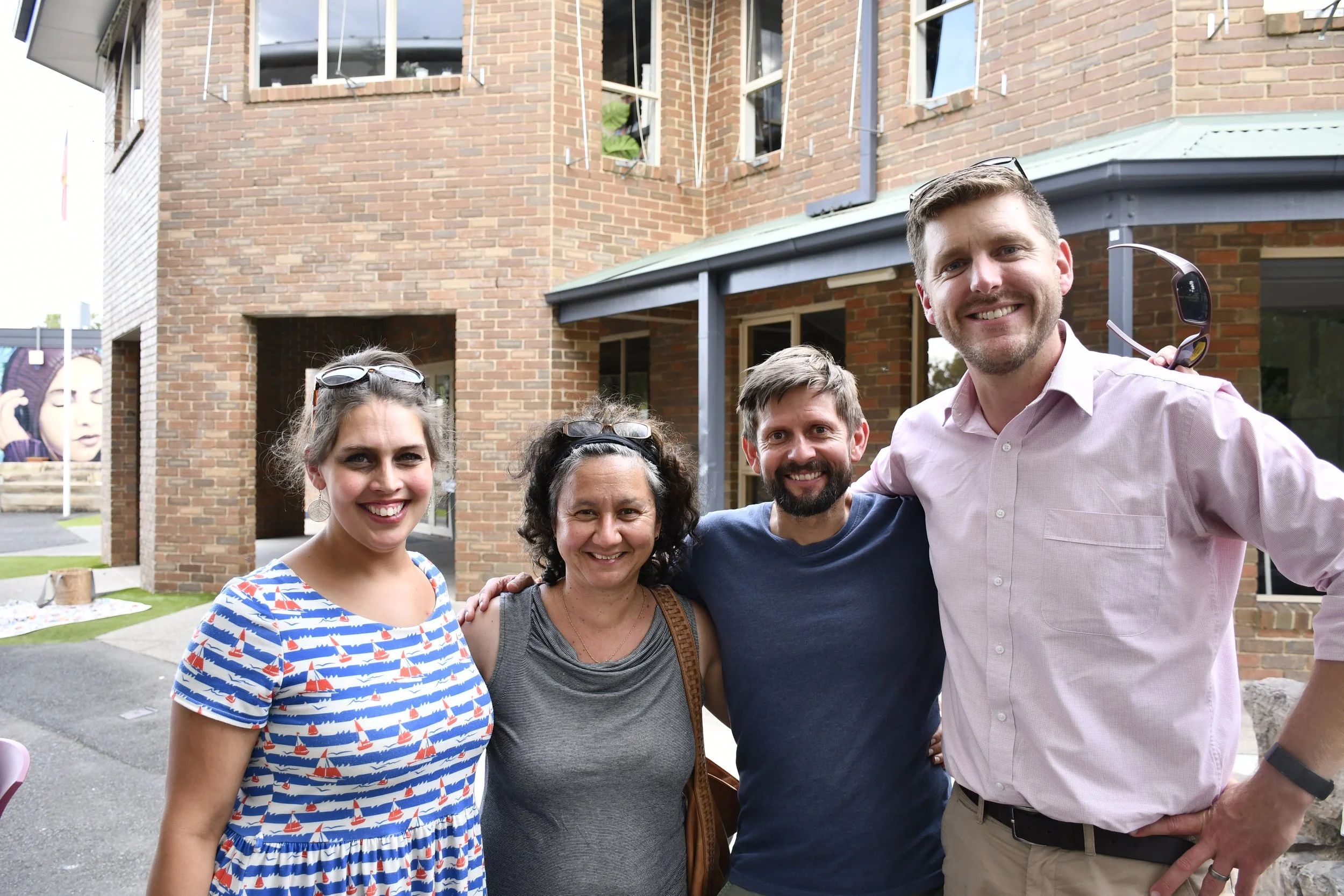 4 parents standing together in a row with their arms around each other, smiling at the camera