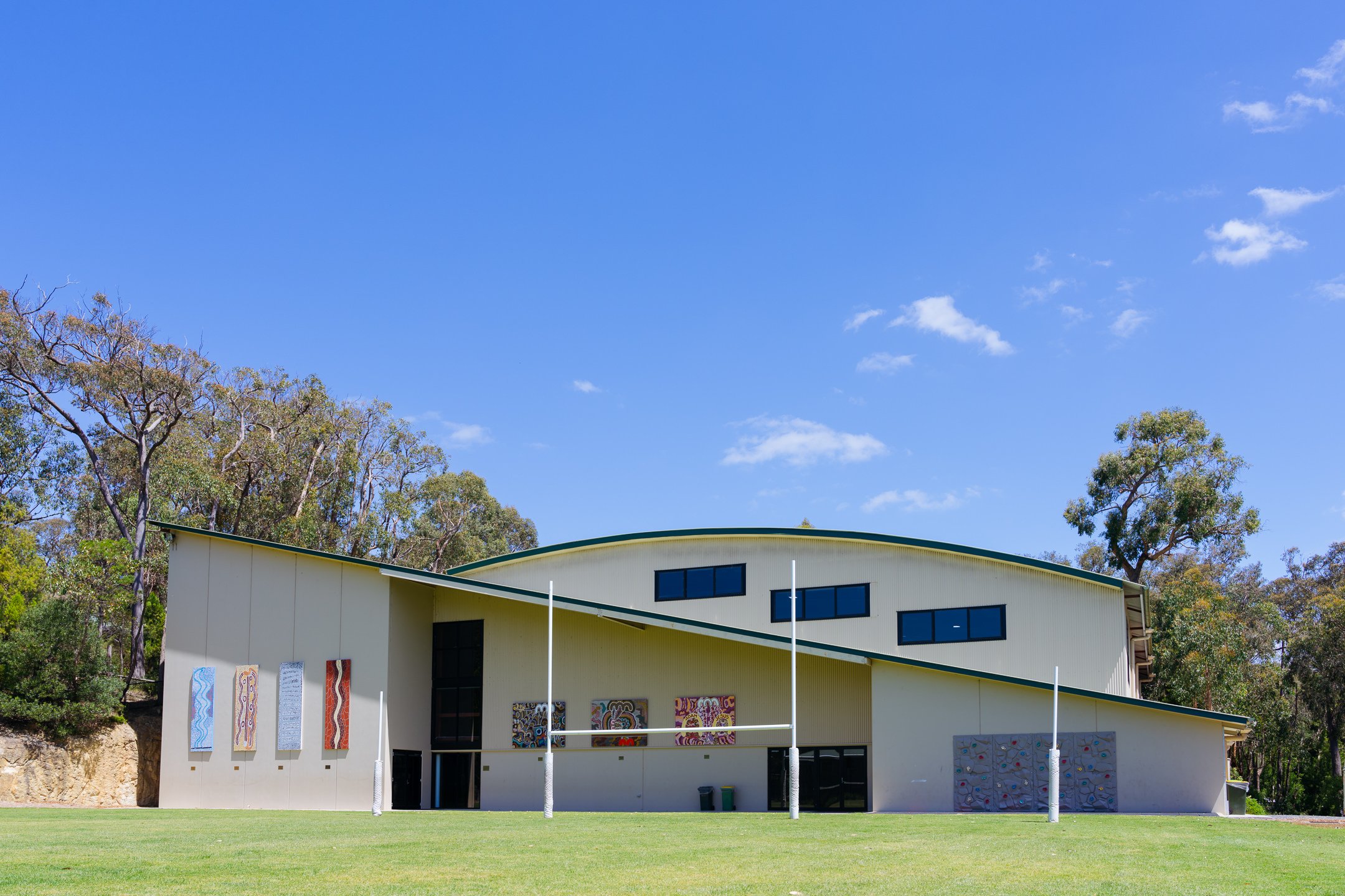 School gymnasium photographed from outside with grass oval in the foreground and blue sky above the roof