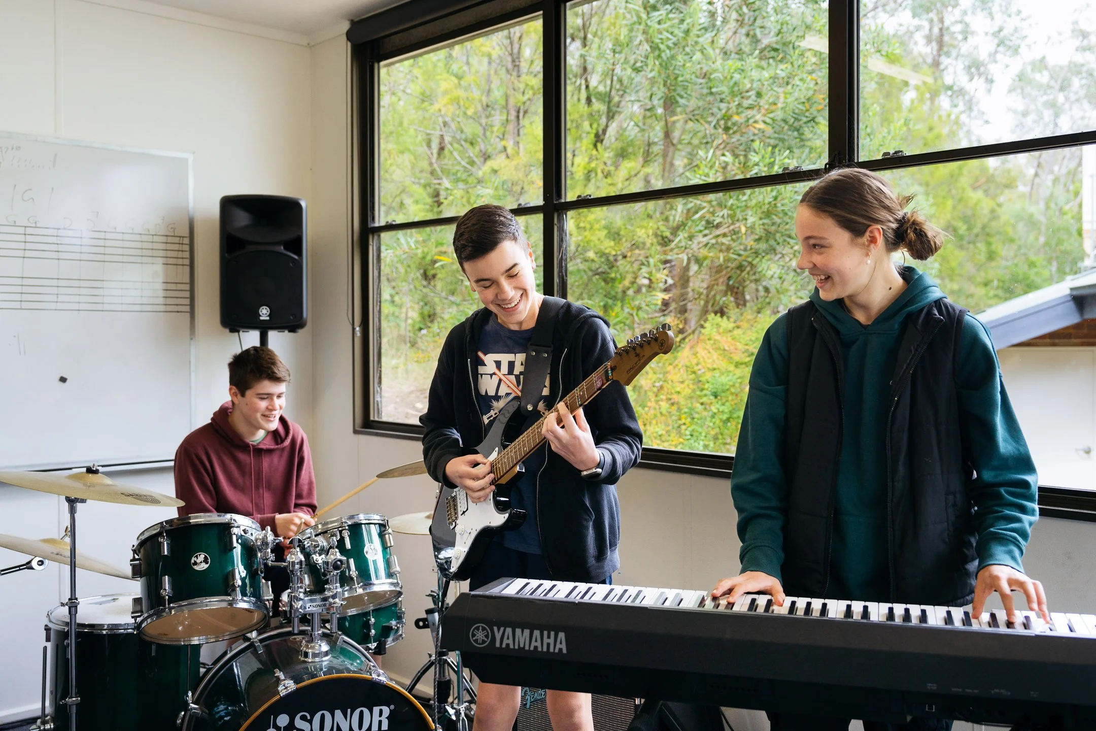 Three students play musical instruments in a classroom