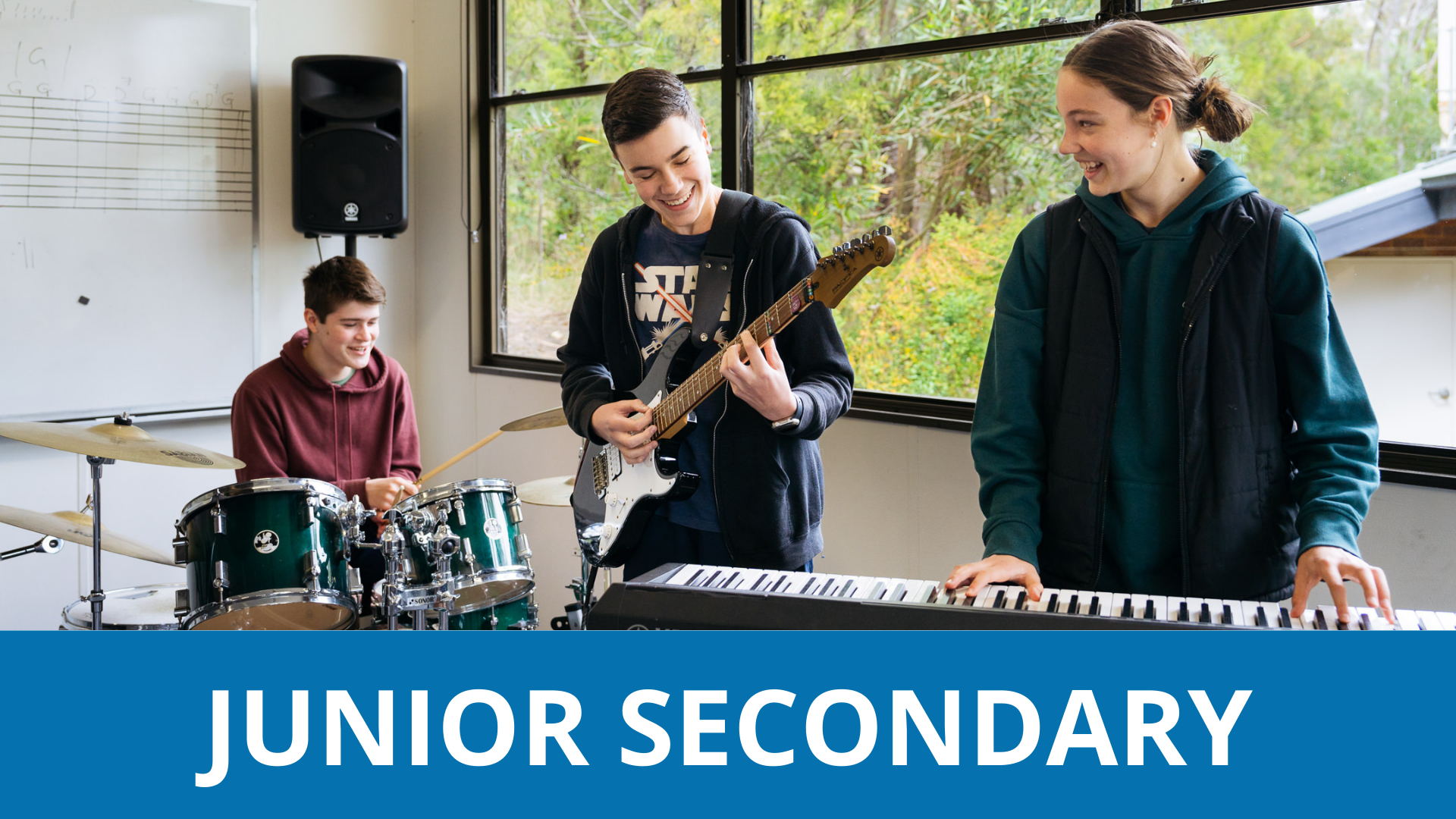 Three Year 9 students playing instruments in a classroom with a blue banner below the image that reads 'Junior Secondary'