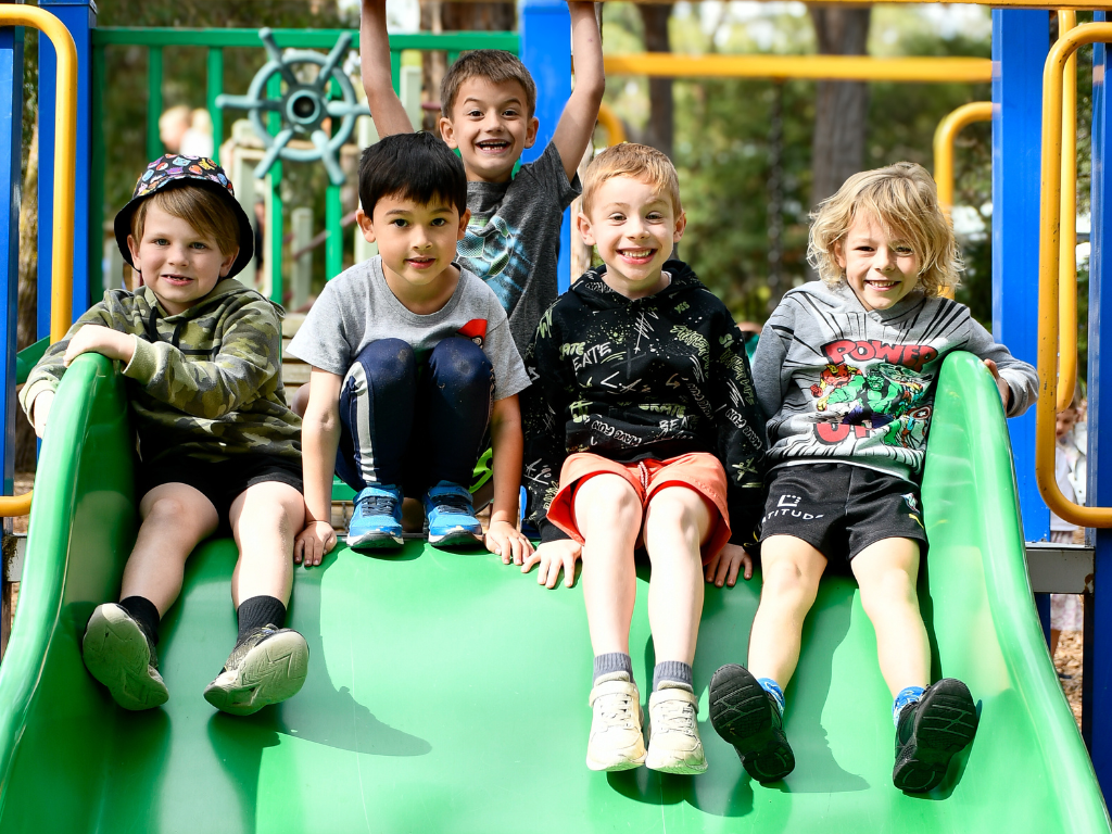 5 male junior primary students seated at top of green slide in playground