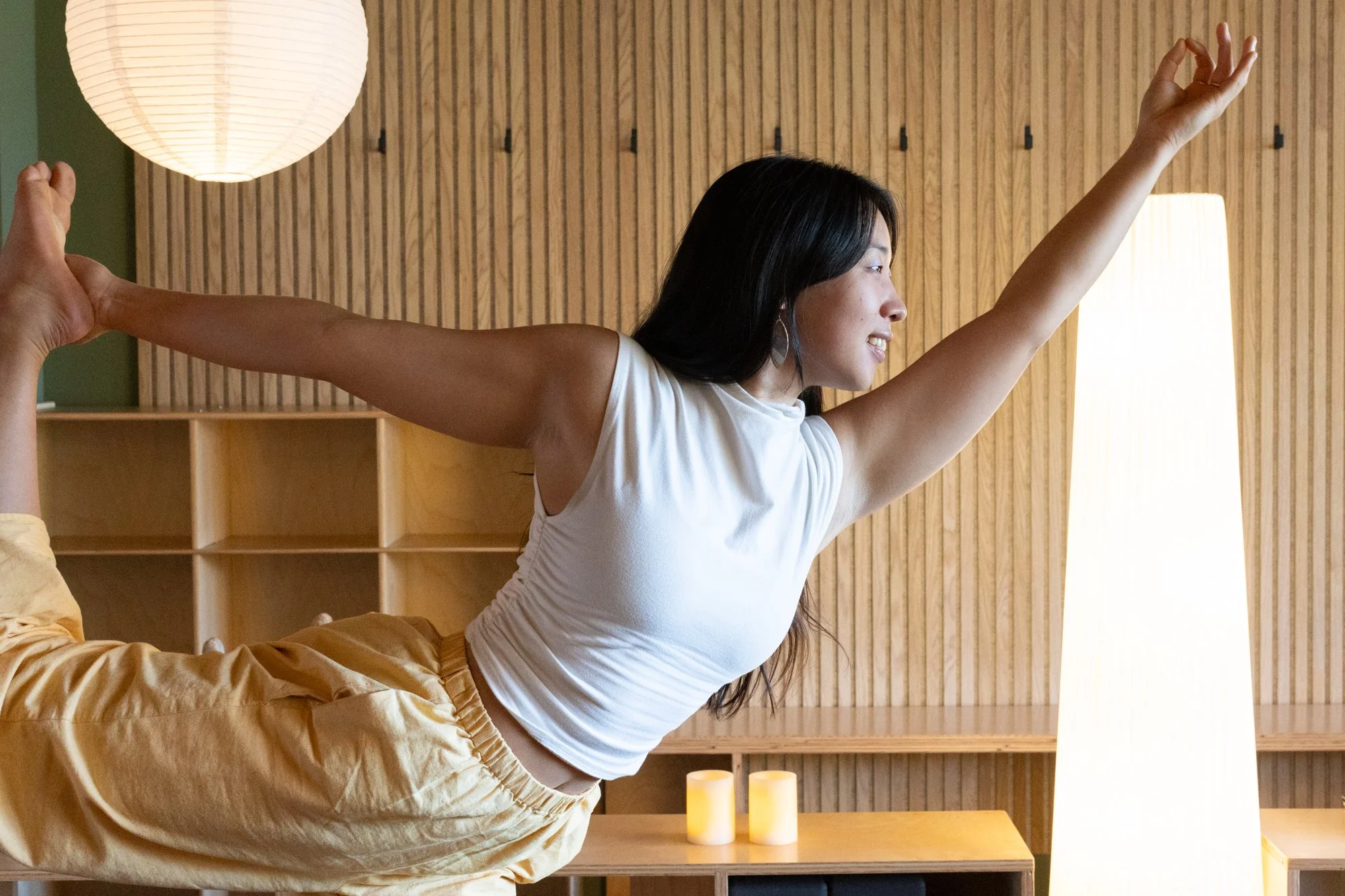 A woman practicing yoga in a lunge pose with arms extended upward in a bright, minimal room.