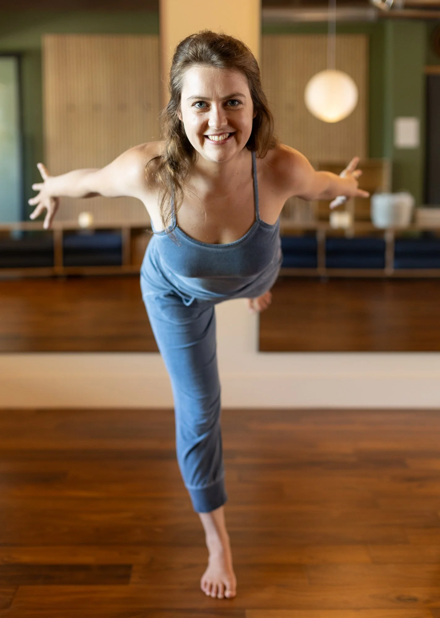 A woman practicing yoga in a lunge pose with arms extended upward in a bright, minimal room.