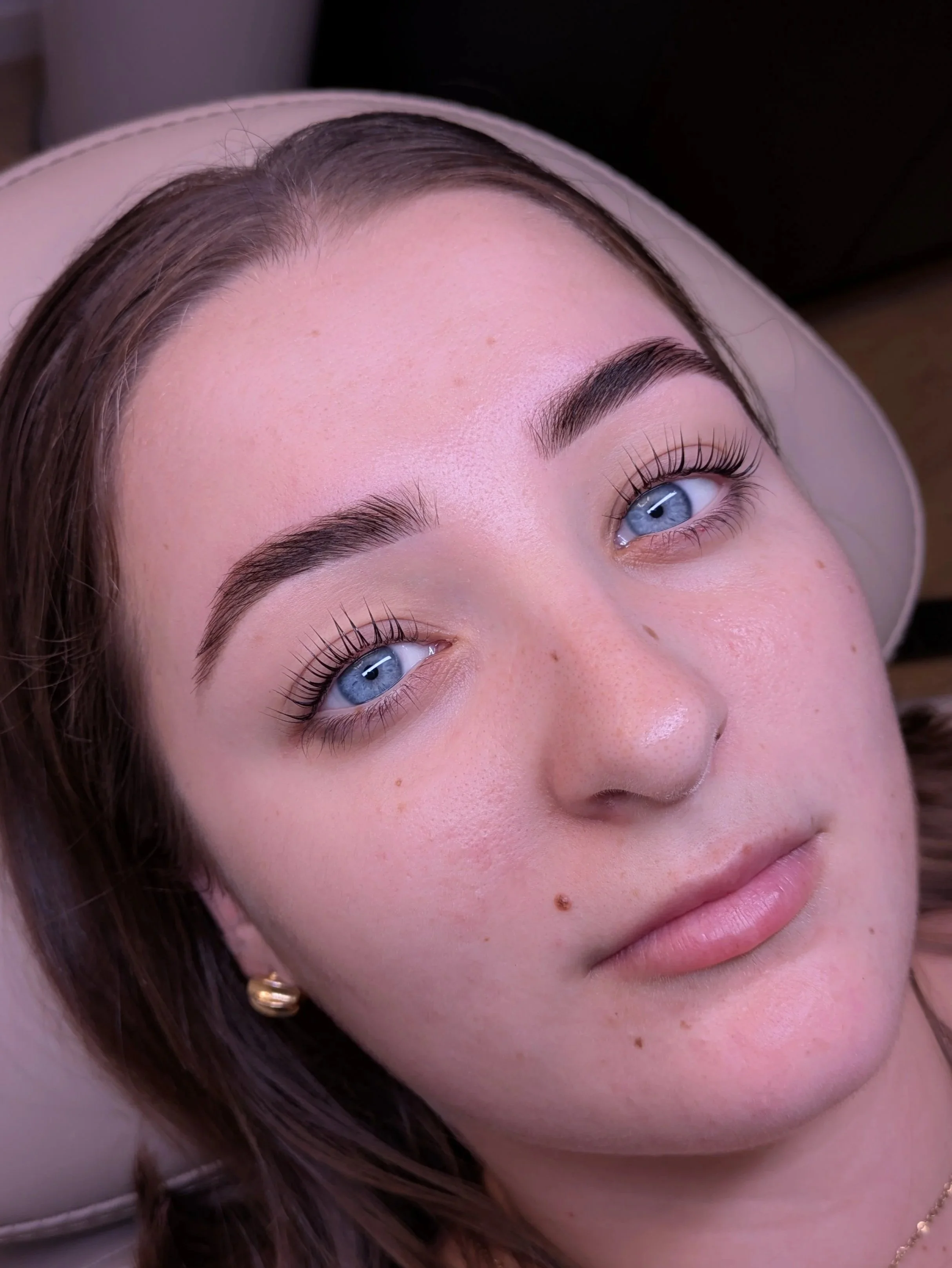 Close-up portrait of a woman with blue eyes, dark hair, defined eyebrows, long eyelashes, freckles, and pink lips.