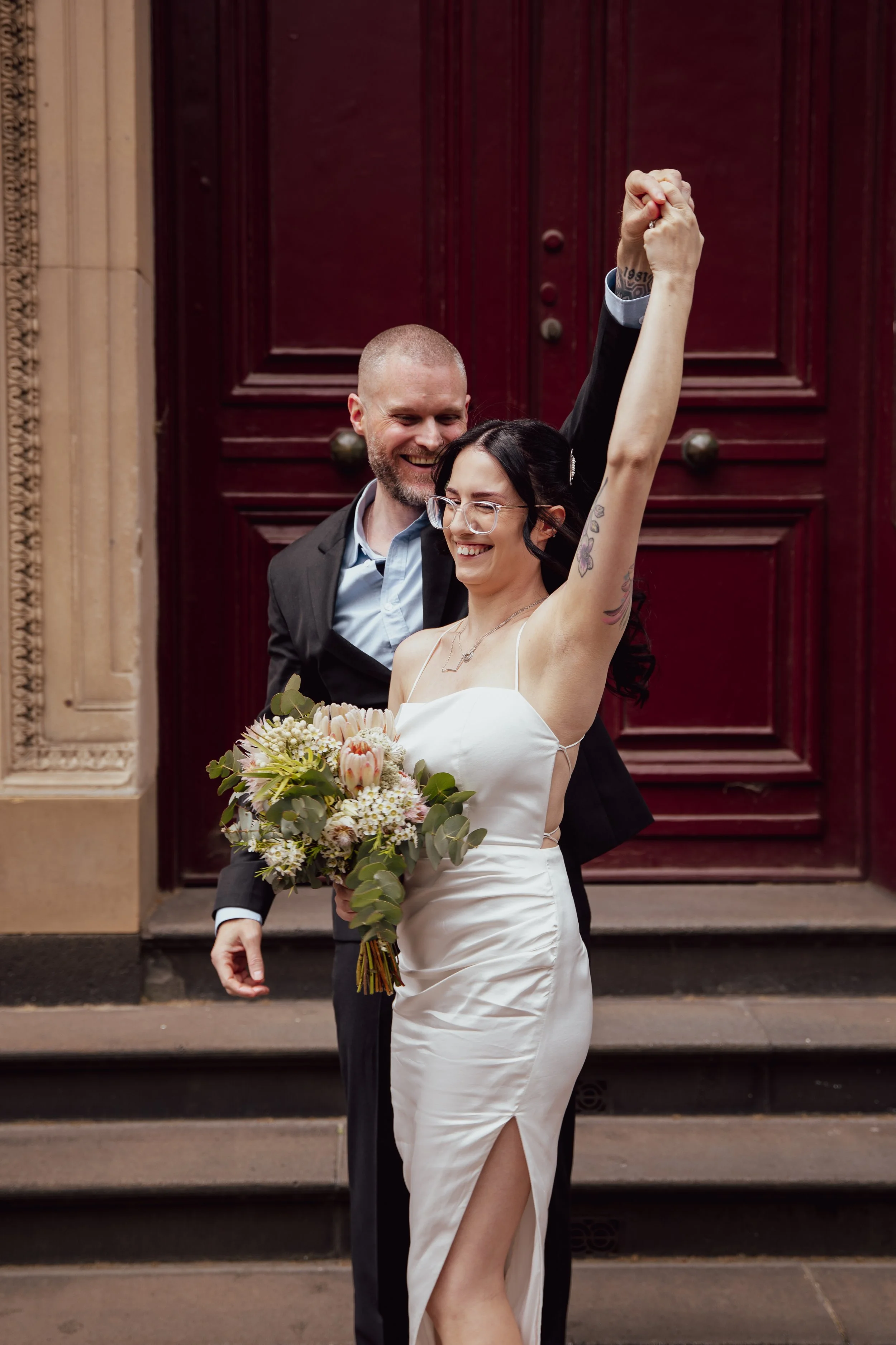 A bride and groom celebrating after wedding, with the bride holding a bouquet and the groom raising his arm in joy.