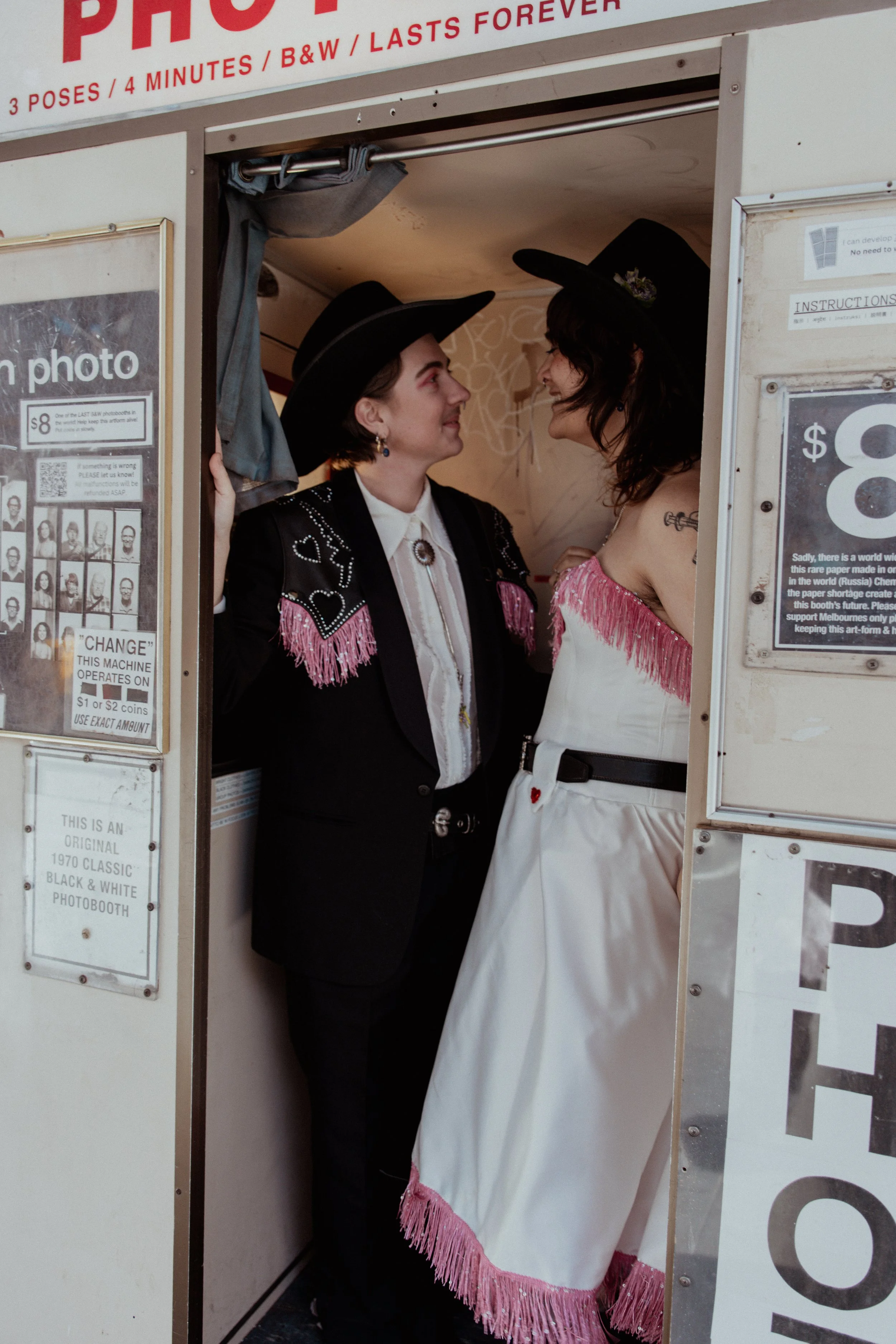 Two women in cowboy hats and western-themed clothing inside a photo booth, facing each other with smiles.