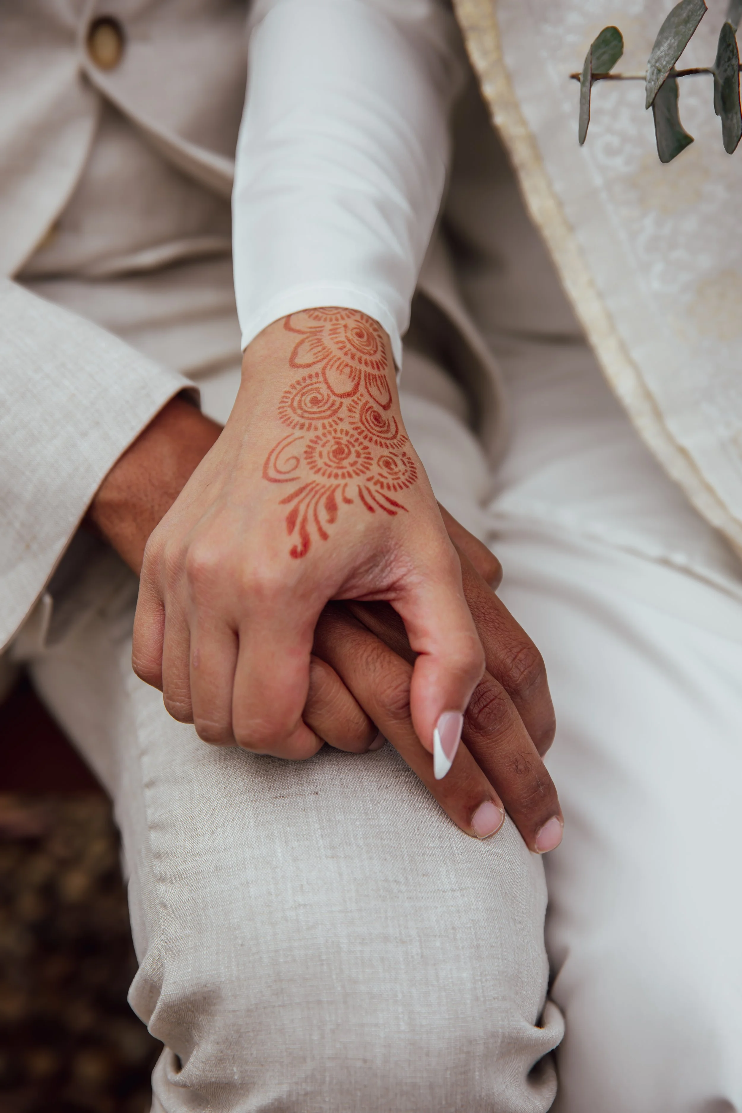 Close-up of a couple holding hands, with the woman showing a henna tattoo on her wrist, dressed in elegant clothing.