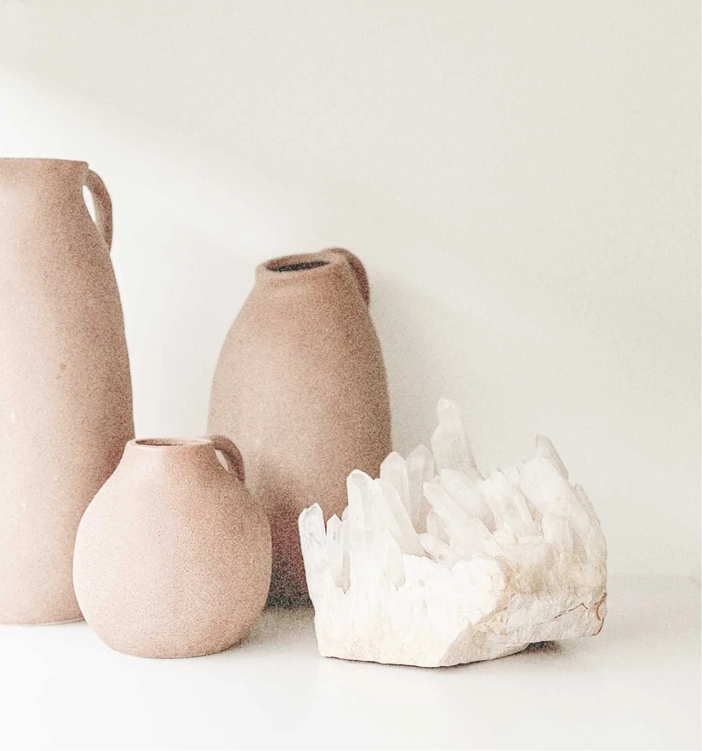 Three beige vases of different sizes next to a white crystal cluster on a white background.