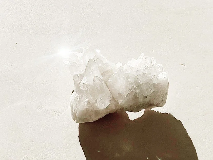 A white quartz crystal cluster on a white surface casting a shadow.