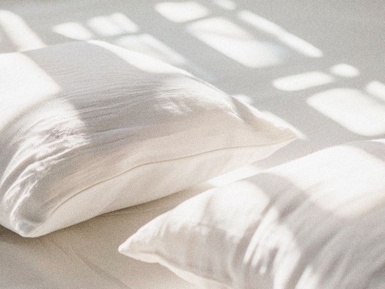 Two white pillows on a bed with sunlight and shadows cast from window blinds