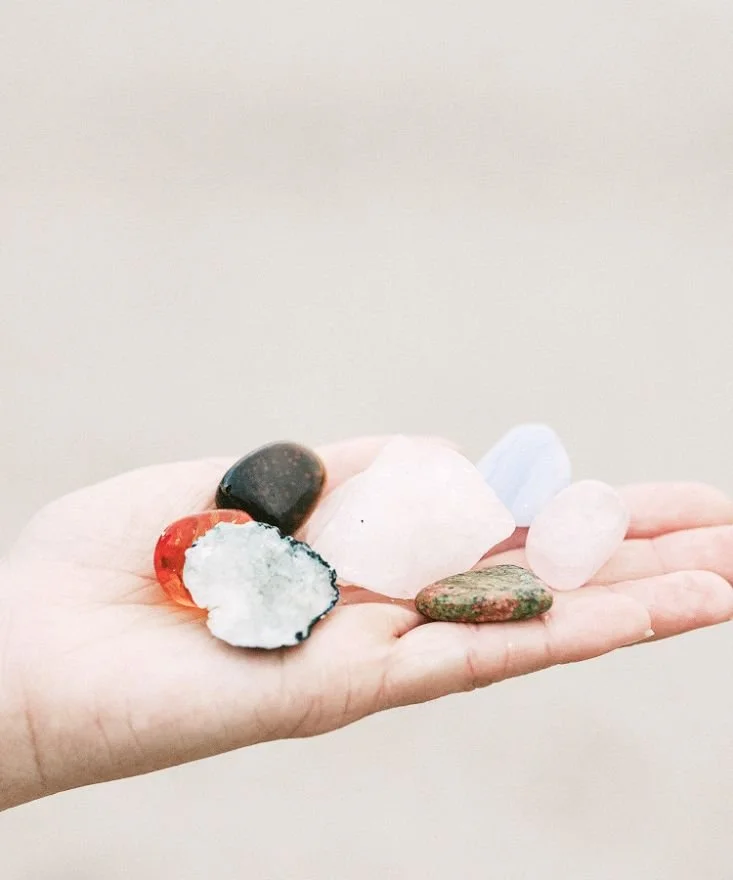 A hand holding various colorful stones and crystals against a plain neutral background.