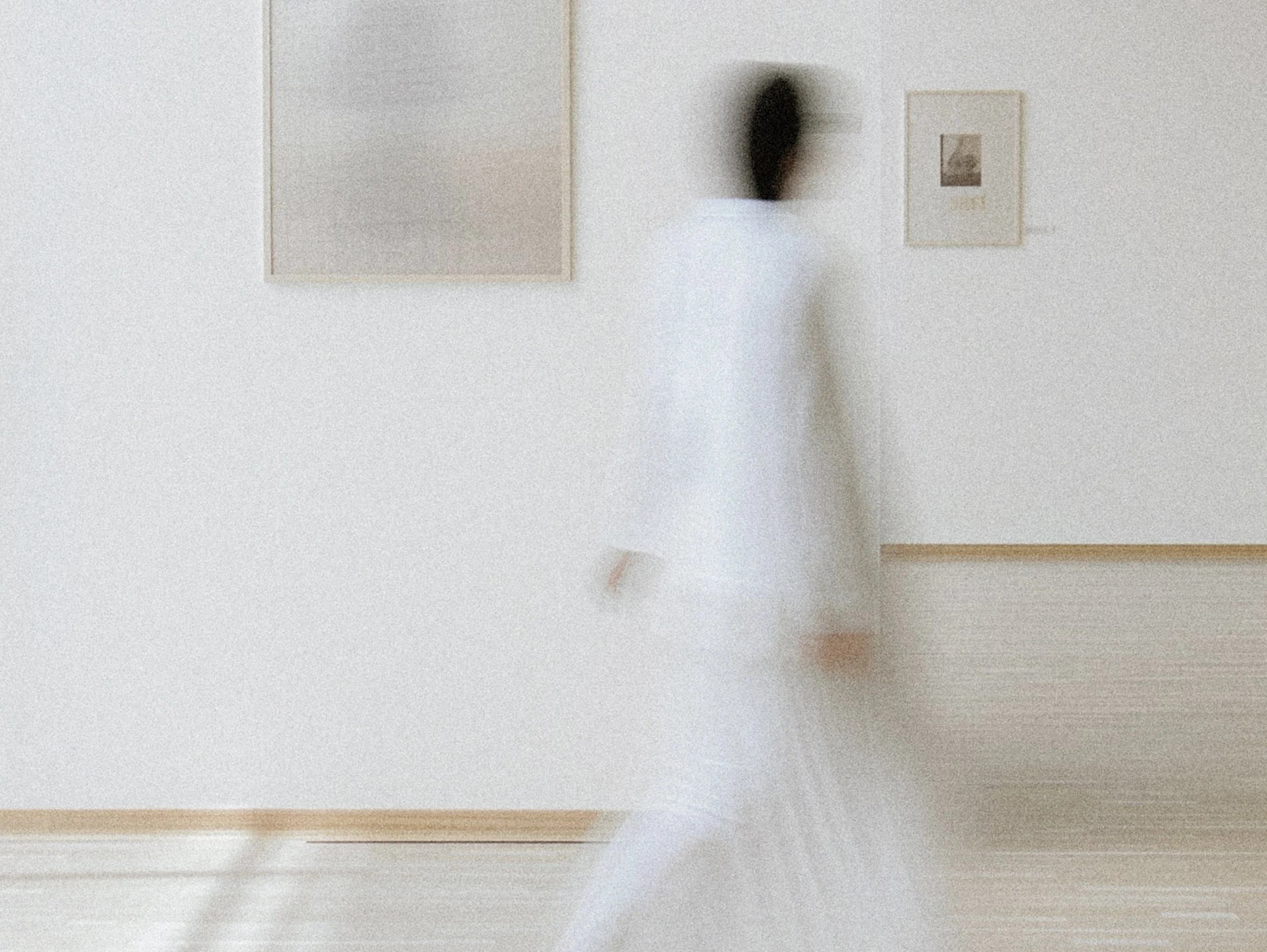 A white wall with framed artwork, a black decorative object, and a wooden floor.