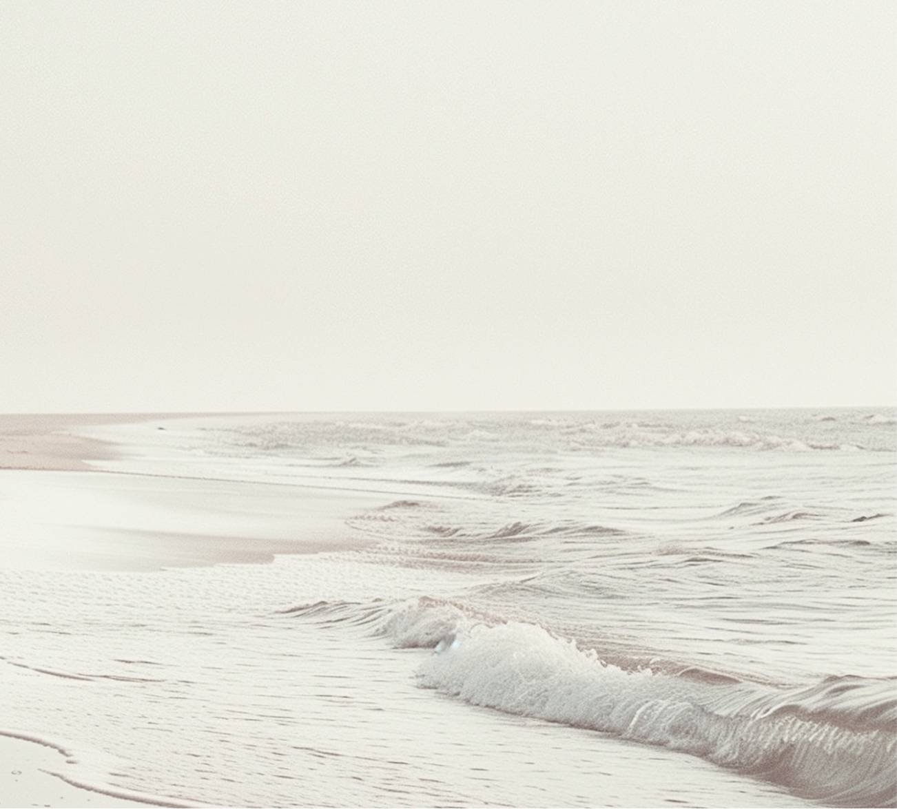 A serene beach scene with gentle waves touching the sandy shore under a light-colored sky.
