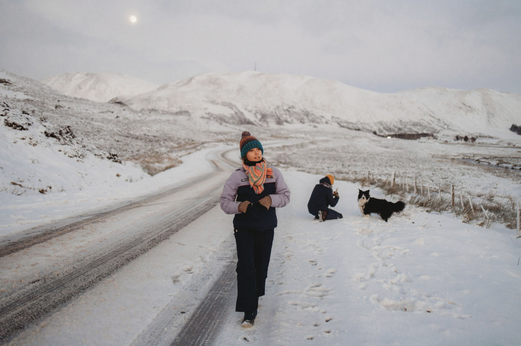 Child and dog standing on a snowy road during the North Coast 500