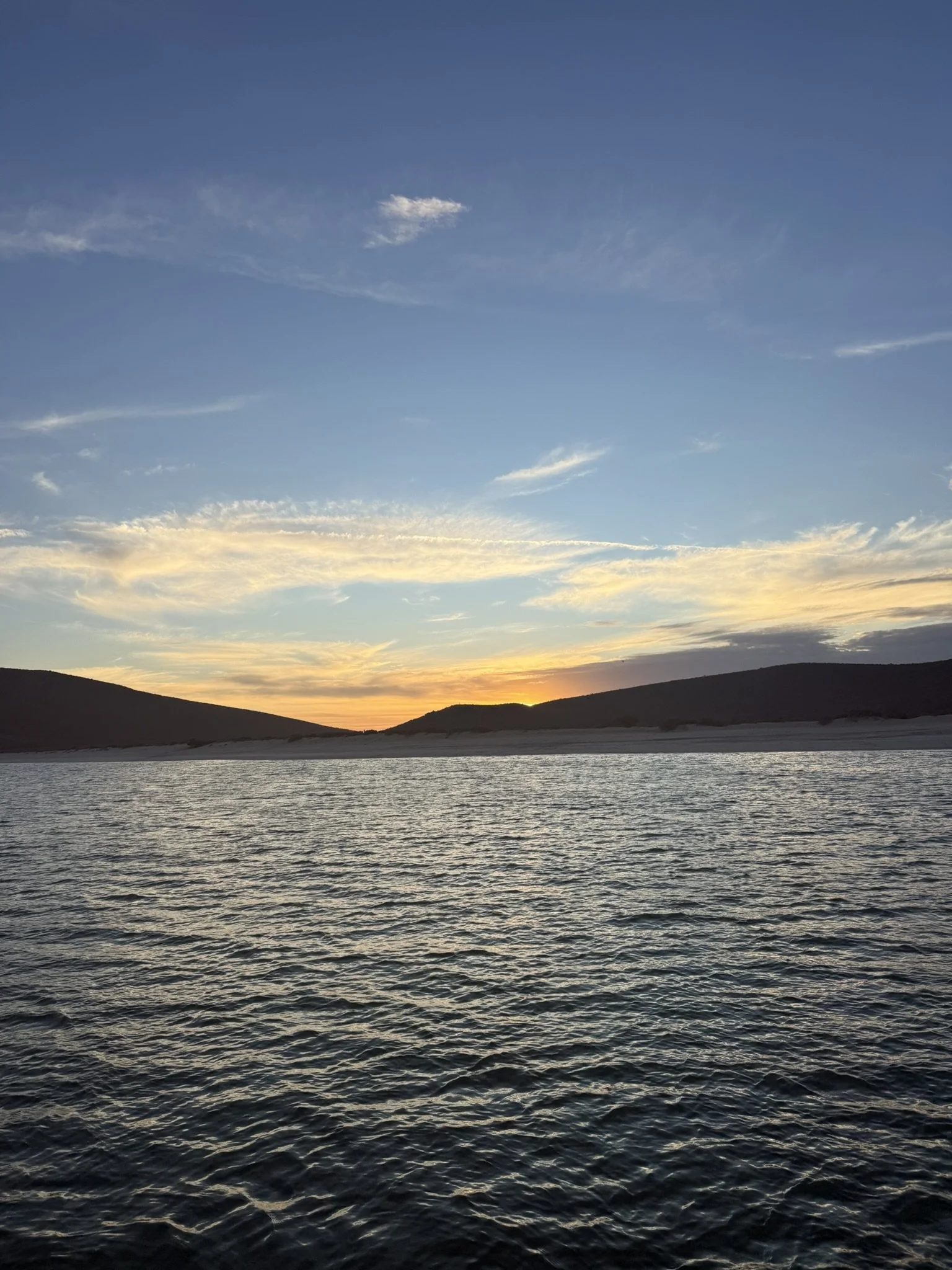Sunset over a body of water with hills in the background and clouds in the sky.