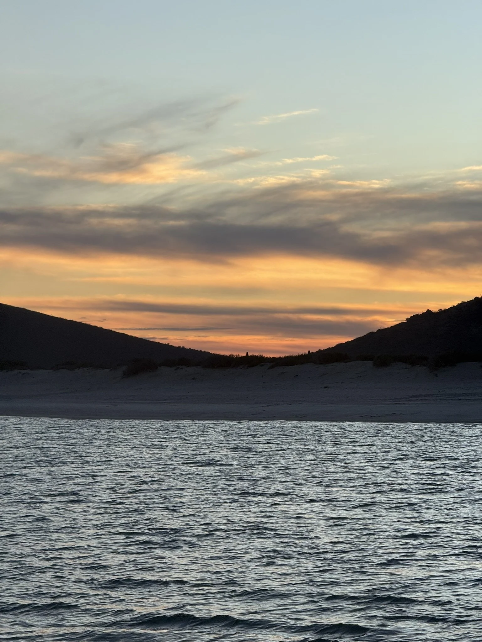 A sunset over the ocean with hills on the horizon and clouds in the sky.