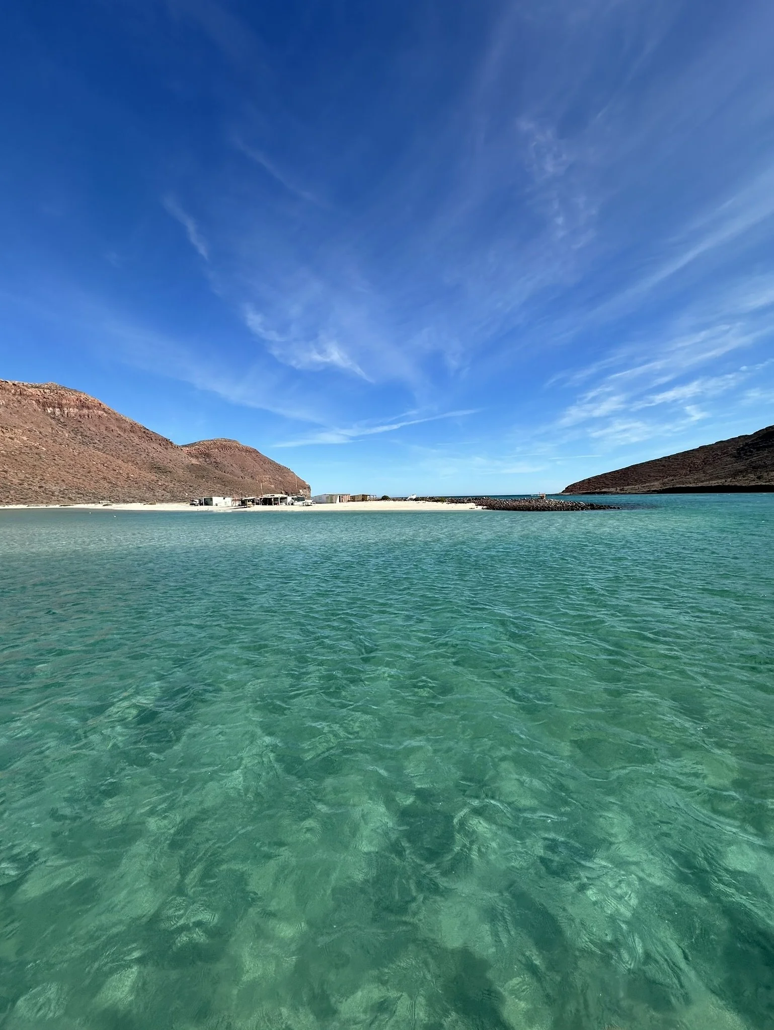Calm turquoise water in a cove with brown hills on either side and a clear blue sky overhead.