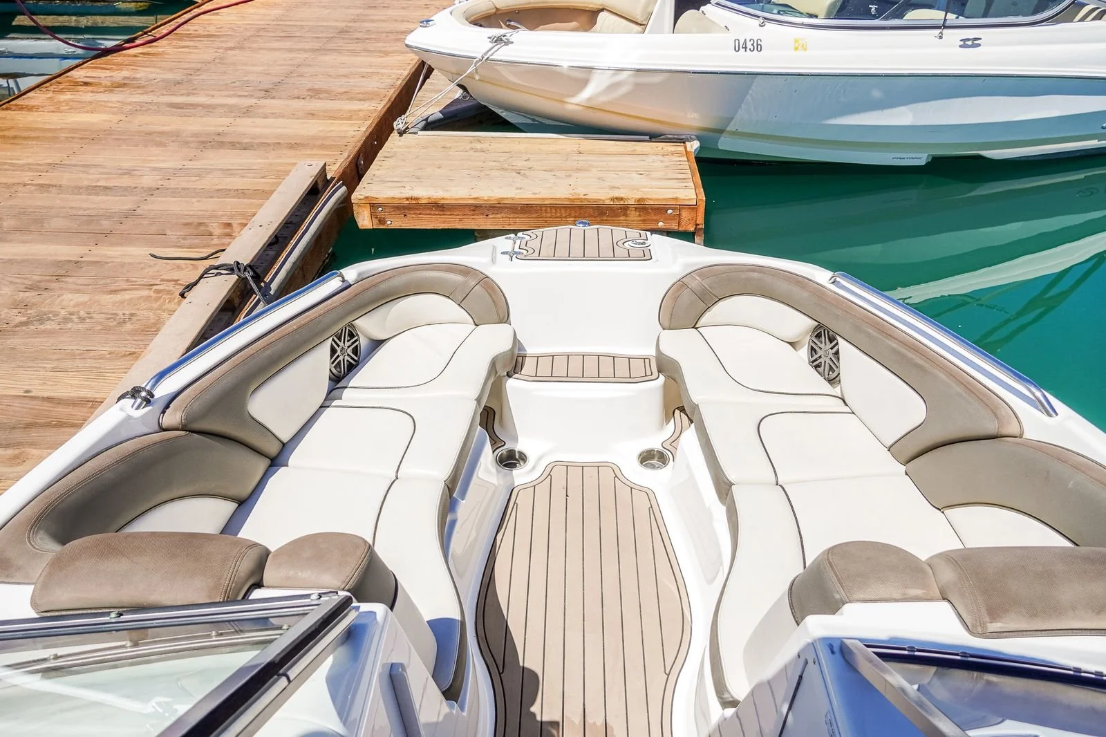 A motorboat docked at a wooden pier, with cushioned seating and a tan and white color scheme, alongside another boat at the dock on calm water.