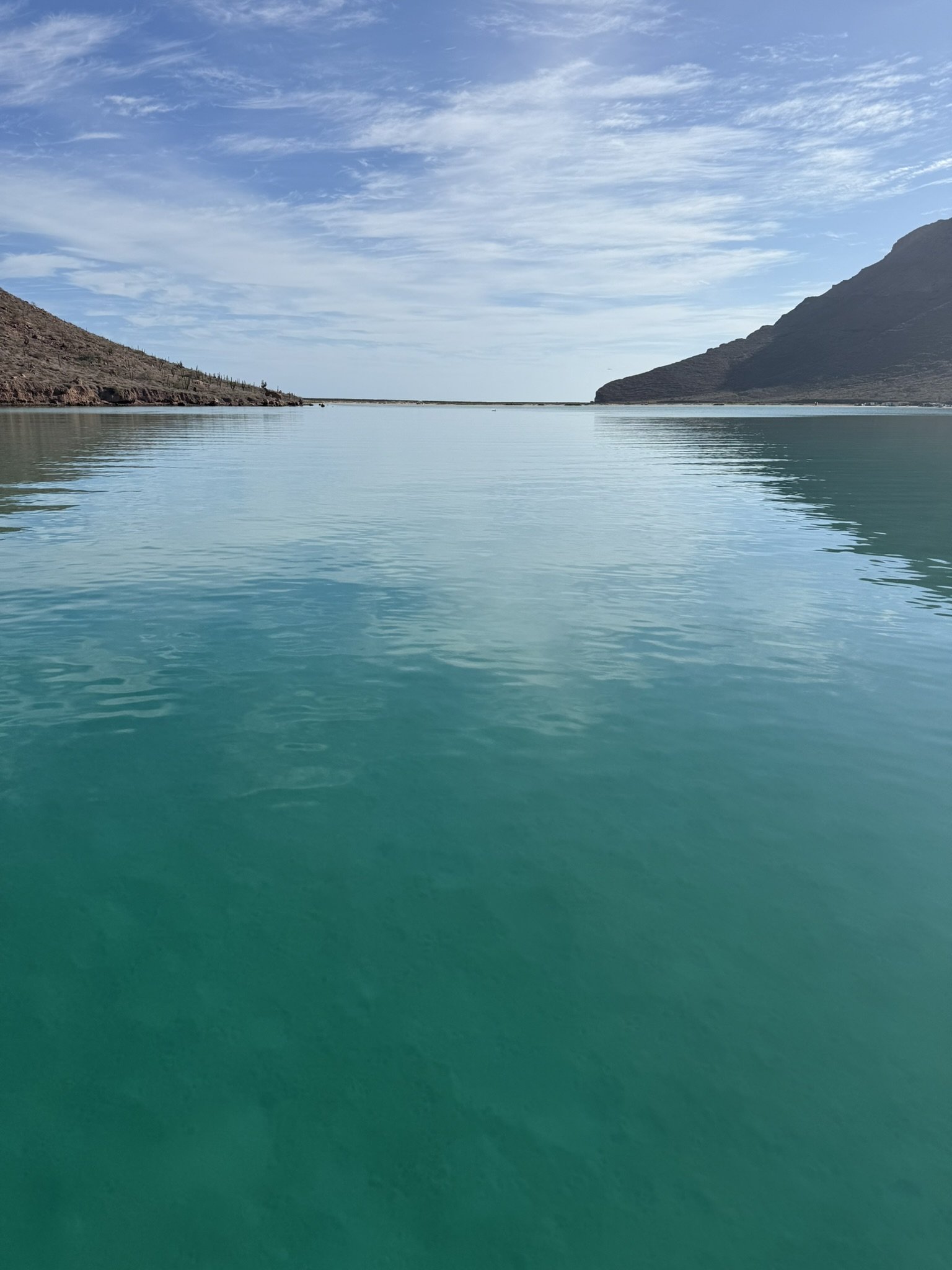 A calm body of turquoise water surrounded by arid desert mountains with a partly cloudy sky.
