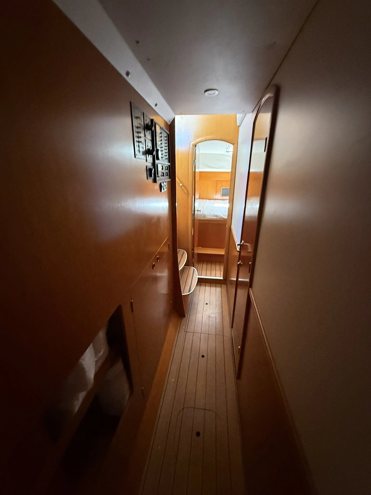 Interior view of a narrow corridor with wood-paneled walls and wooden flooring, leading to a door with a window, and a mirror on the right side.