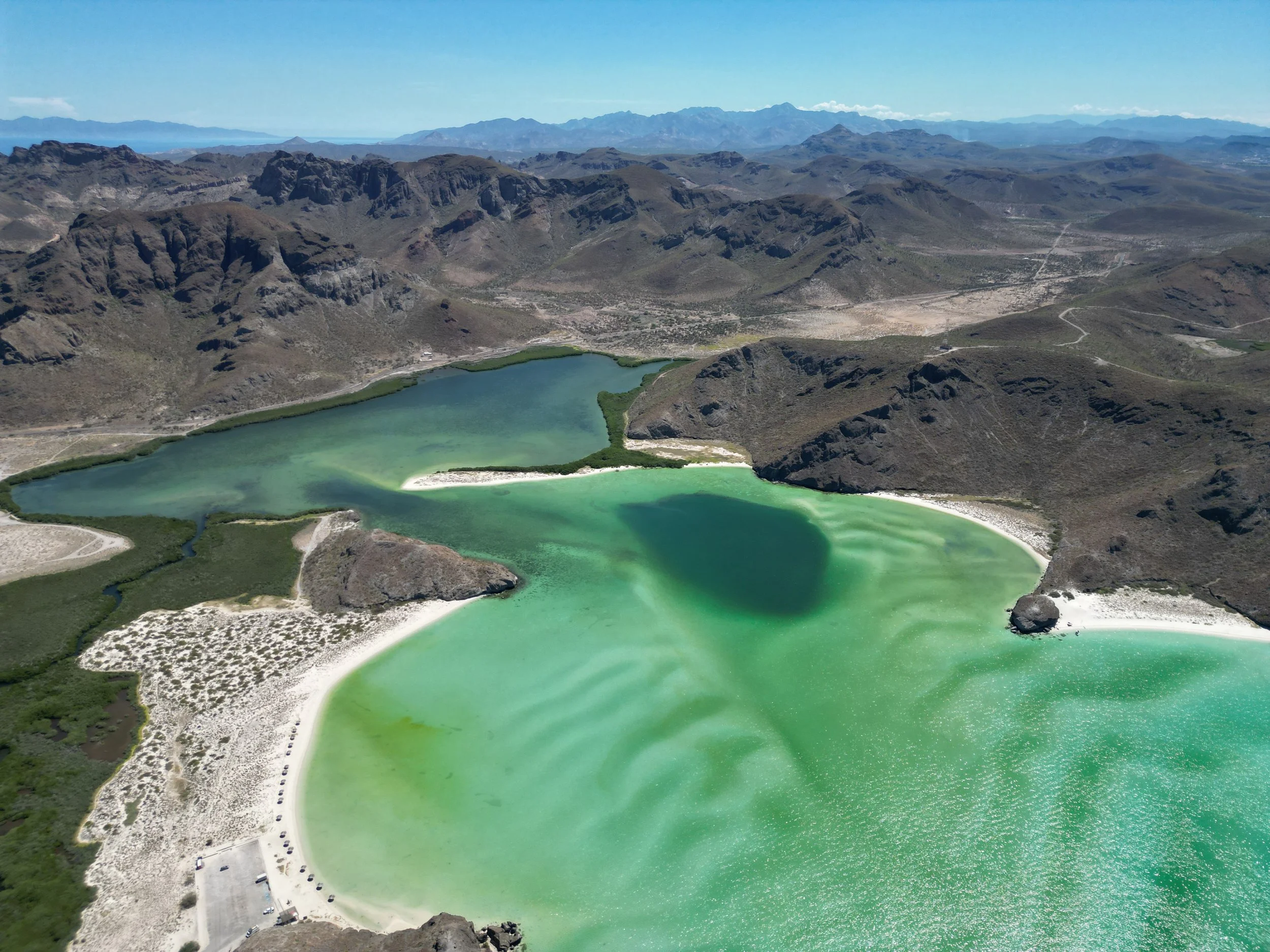 An aerial view of a green-colored lake surrounded by mountains and a small area with parked cars and structures.