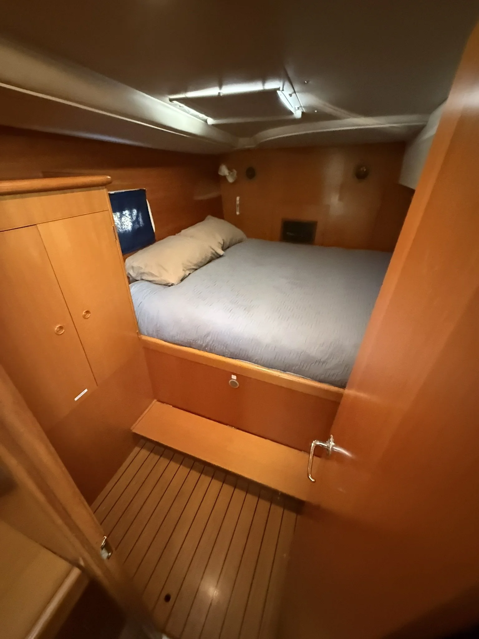Small wooden bedroom with a bed, pillow, and a small window, inside a boat cabin.