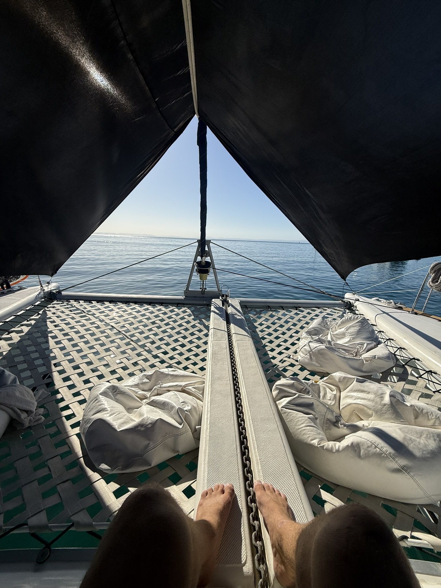 View from the deck of a catamaran boat showing the bow, with a chain and a slide, surrounded by life jackets, with water and distant land in the background.