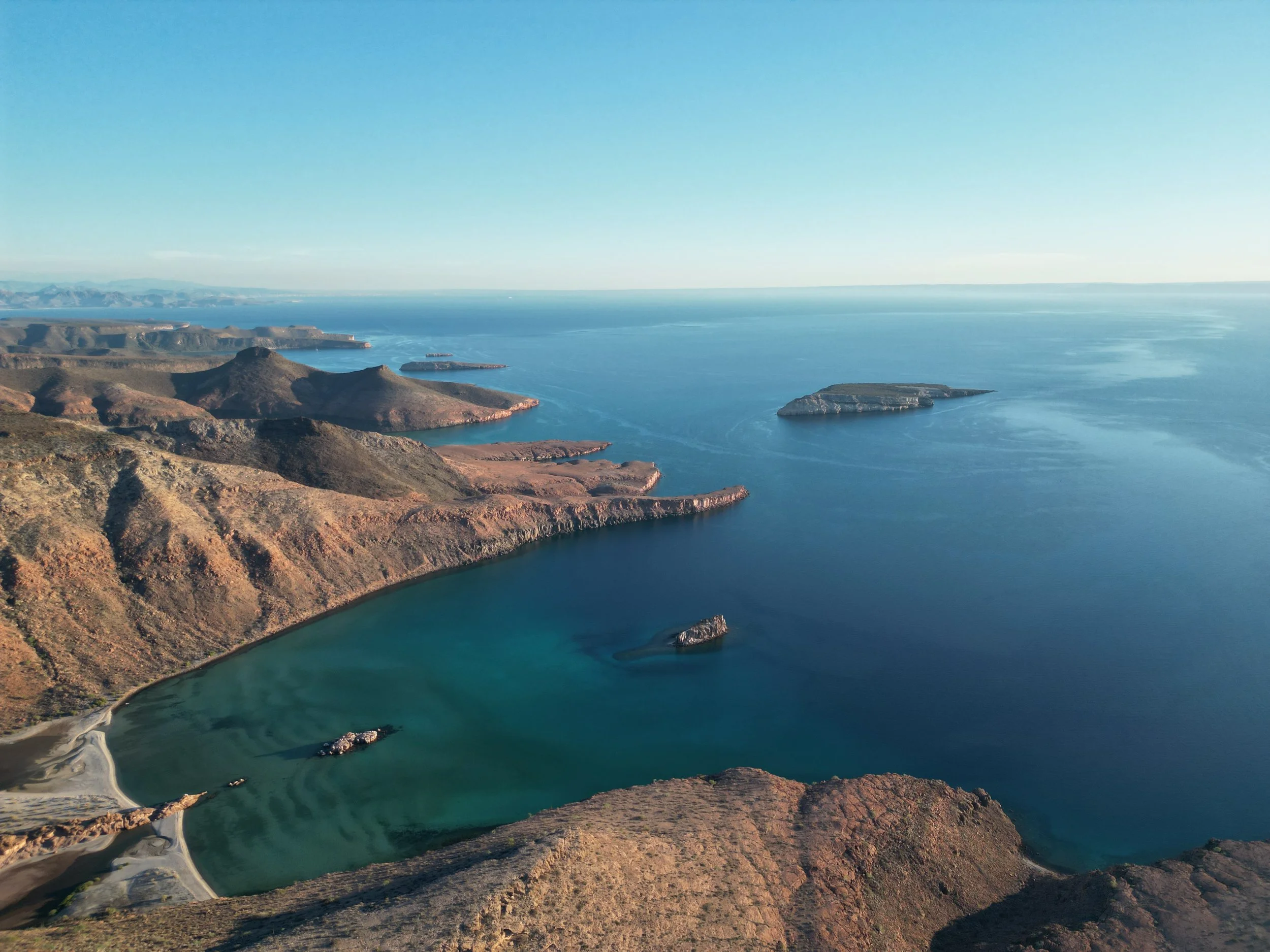 A view of a large body of water surrounded by rocky, mountainous terrain under a clear sky.