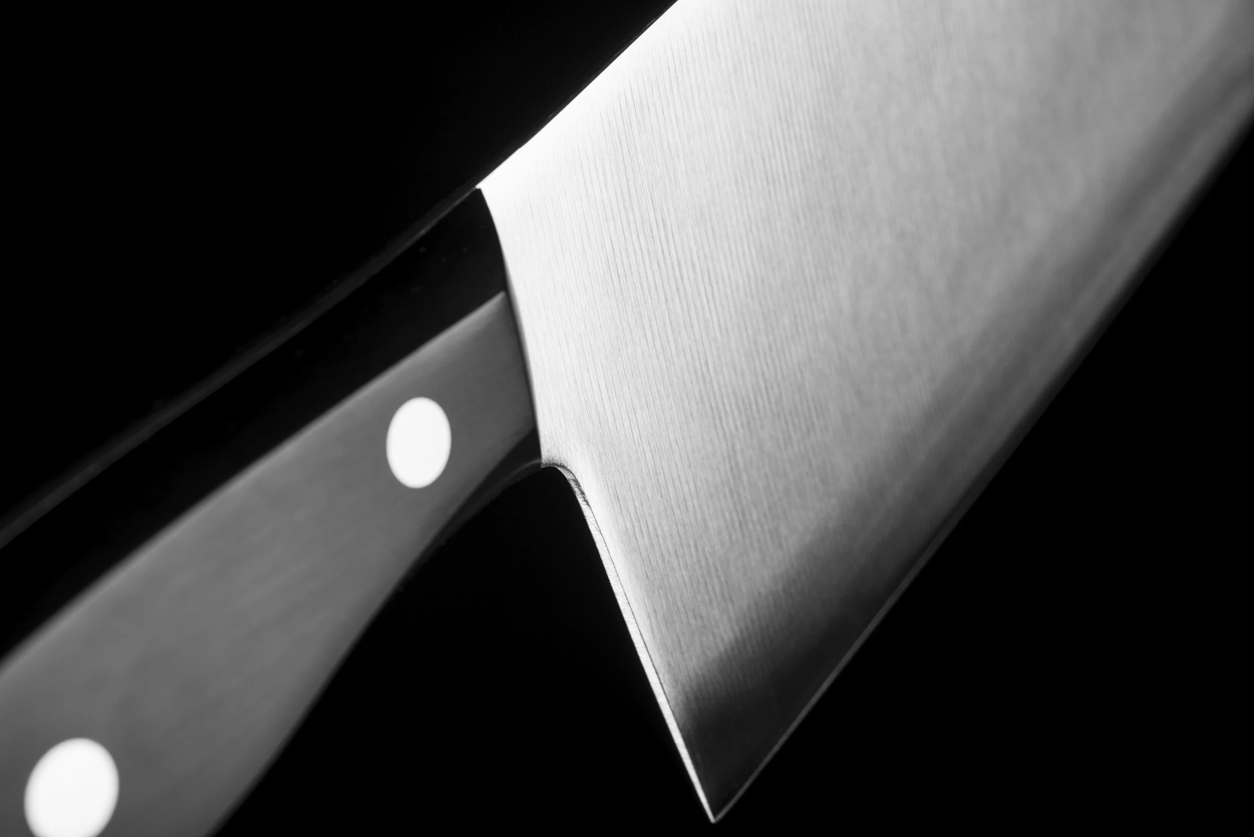 Close-up of a shiny, metallic chef's knife with a textured handle, set against a black background.