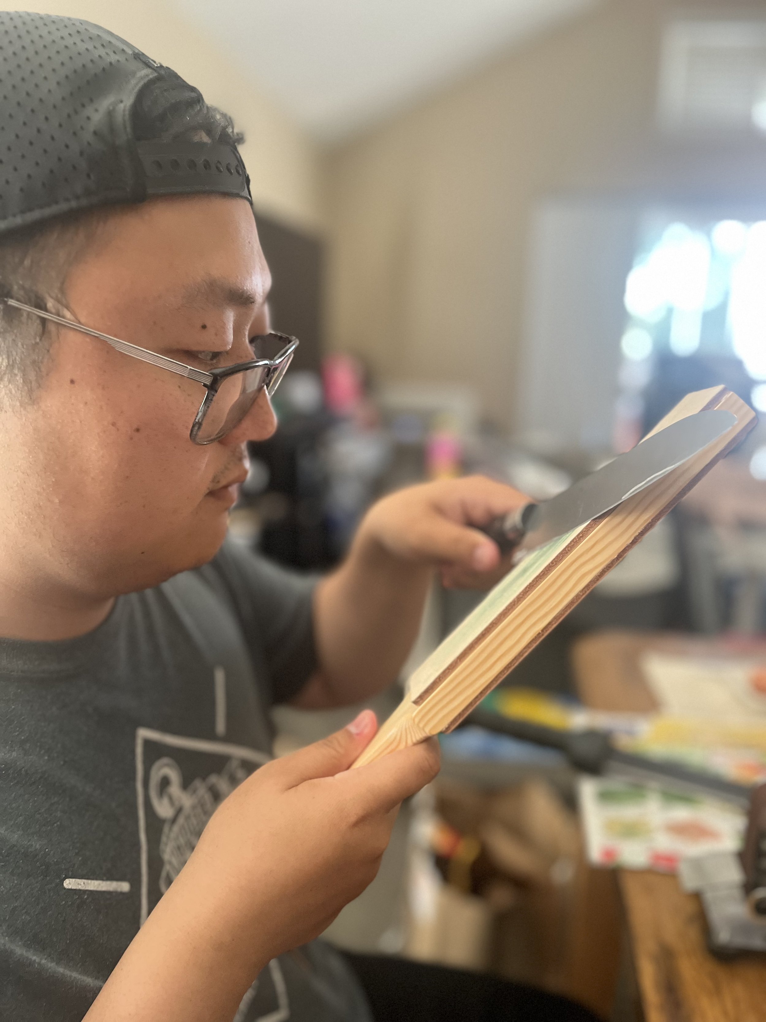 A young man with glasses and a backwards baseball cap is sharpening a knife on a leather strop for a fine tune for a sharp blade.
