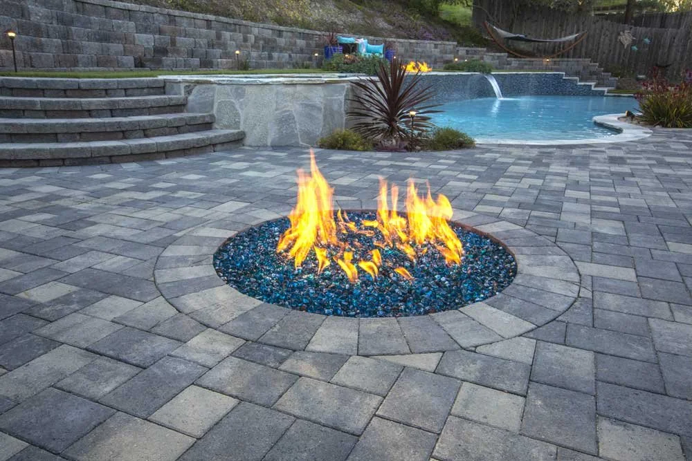 Modern front entrance with large concrete stepping stones, decorative black pebbles, and drought-tolerant greenery near a house with stone accents.