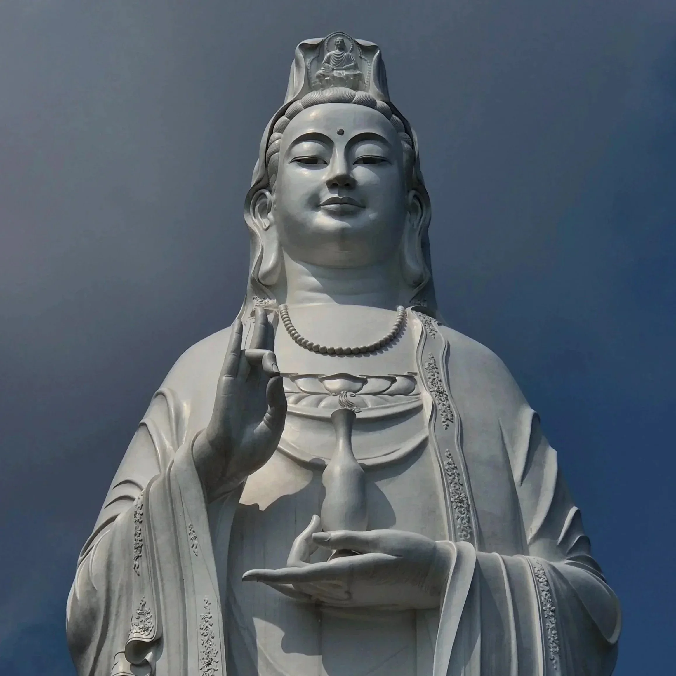 A large white statue of a goddess with a calm expression, holding a vase, with a background of a clear sky.