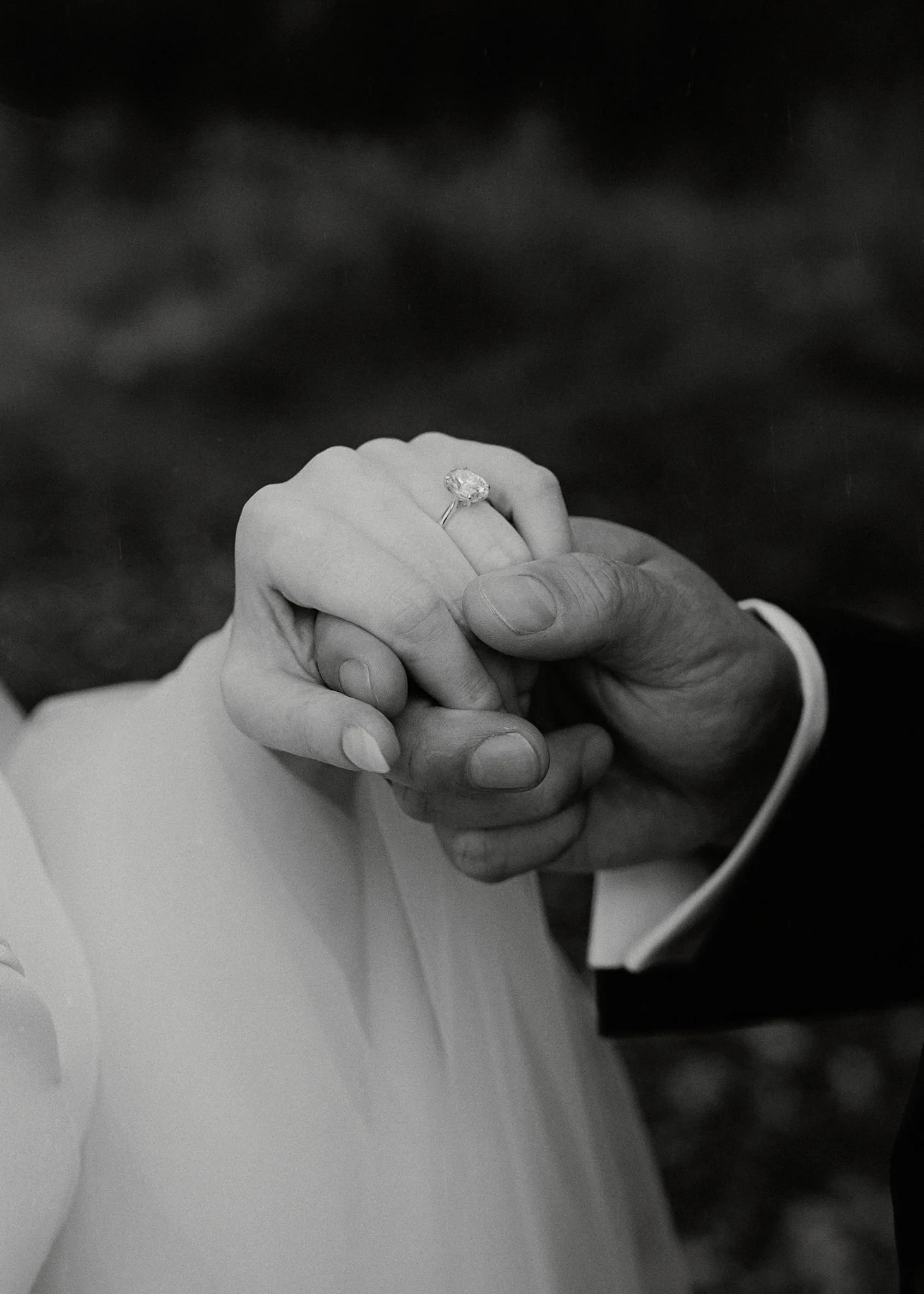 Close-up of a couple holding hands, with the woman's hand displaying an engagement ring.