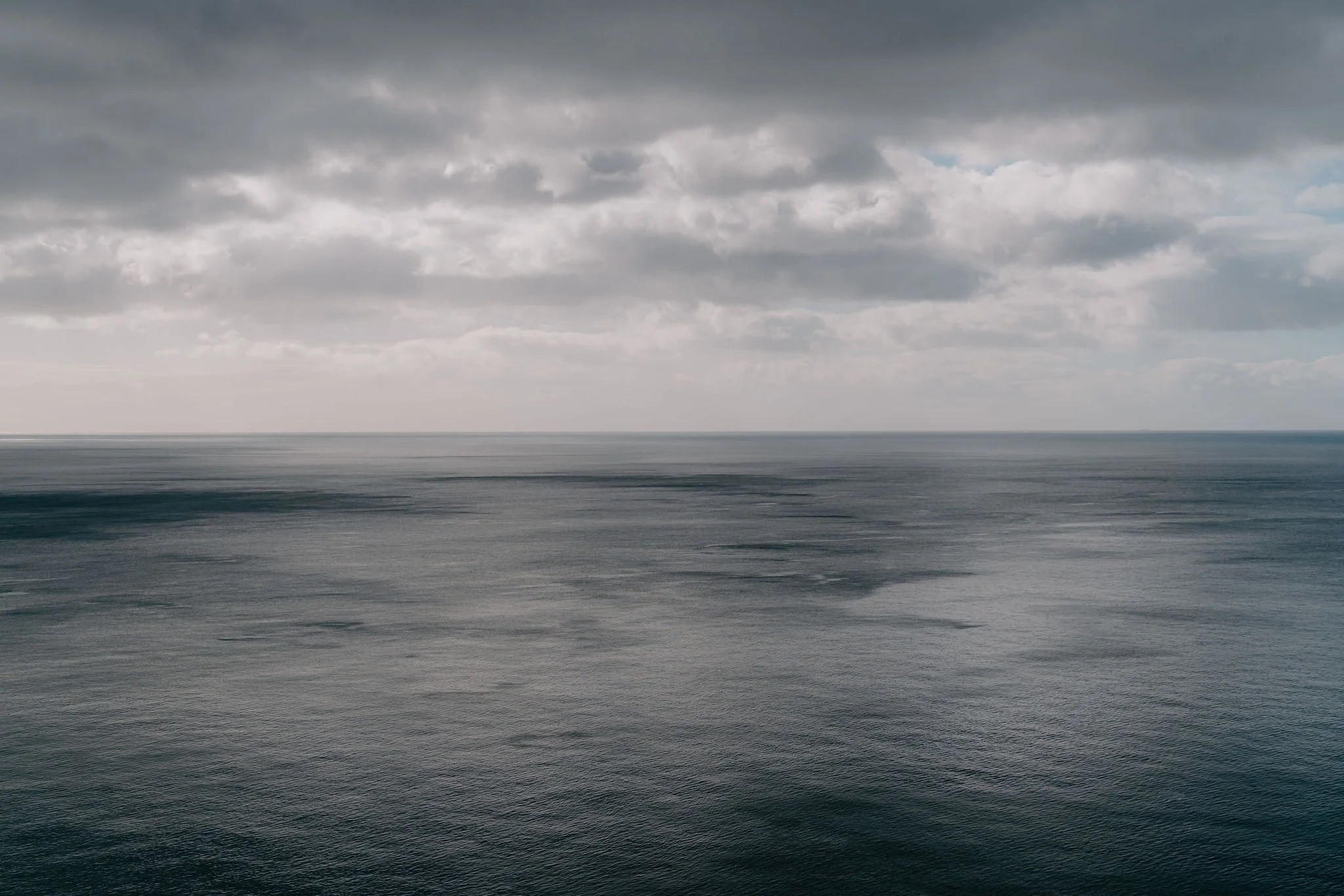 Overcast sky over a calm ocean with subtle waves and a distant horizon.