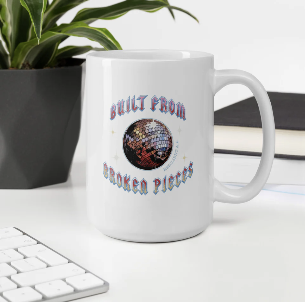 Image of a desk with a white mug that says "Built from Broken Pieces" and a disco ball. 