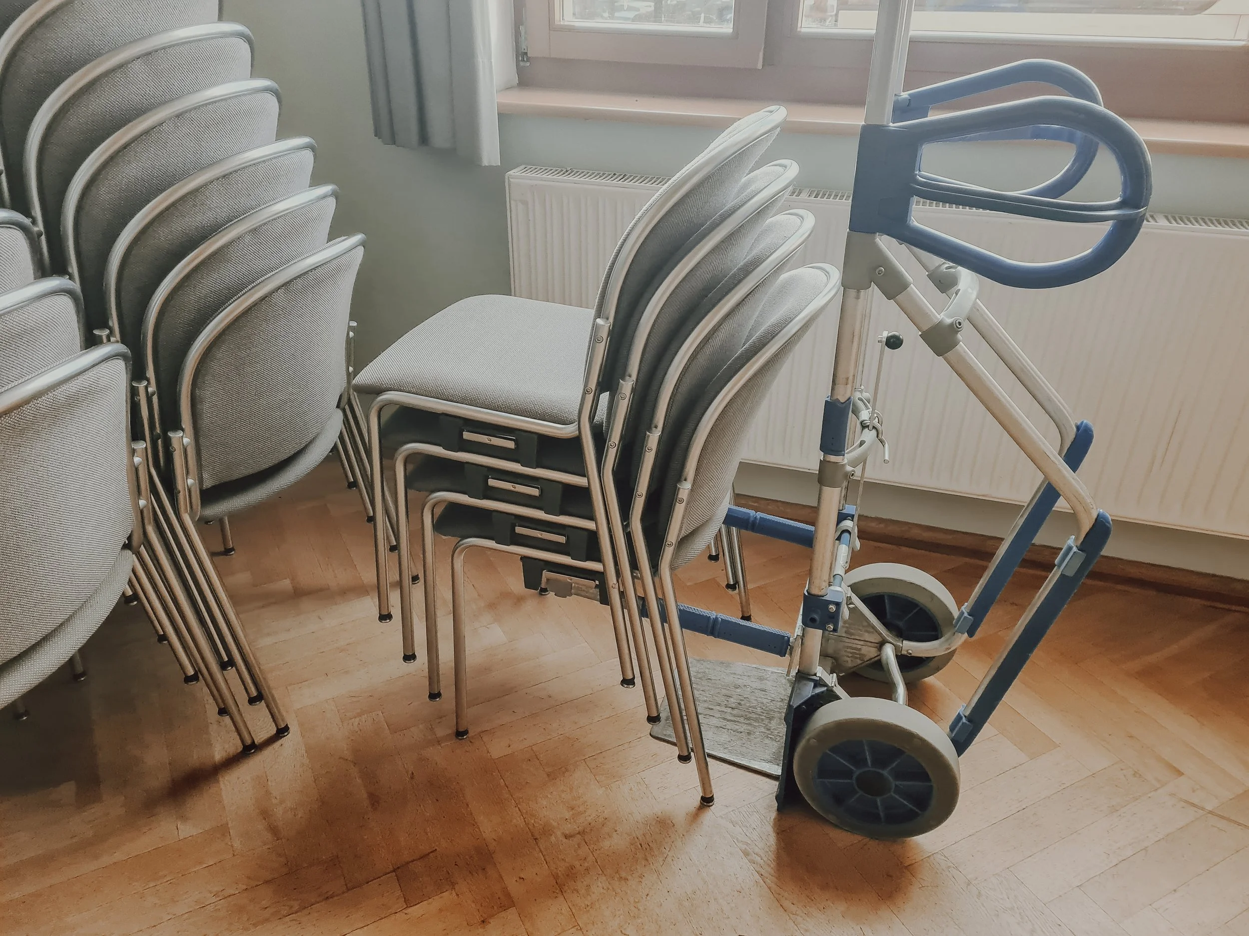 Mehrere Stühle, ein Rollator und ein Fenster in einem Raum mit Holzboden.