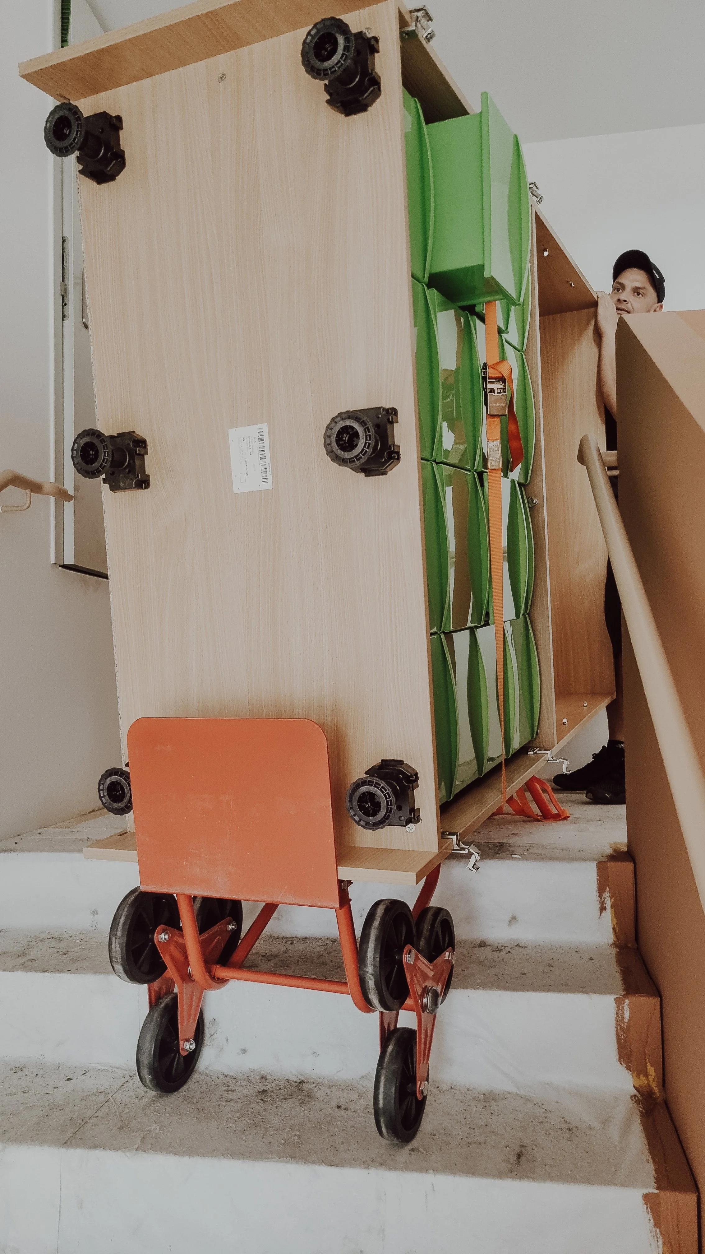 Ein umgedrehter Holzwagen mit grünen und orangefarbenen Aufsätzen, der auf einem Boden steht, mit einer Person, die im Hintergrund teilweise sichtbar ist.
