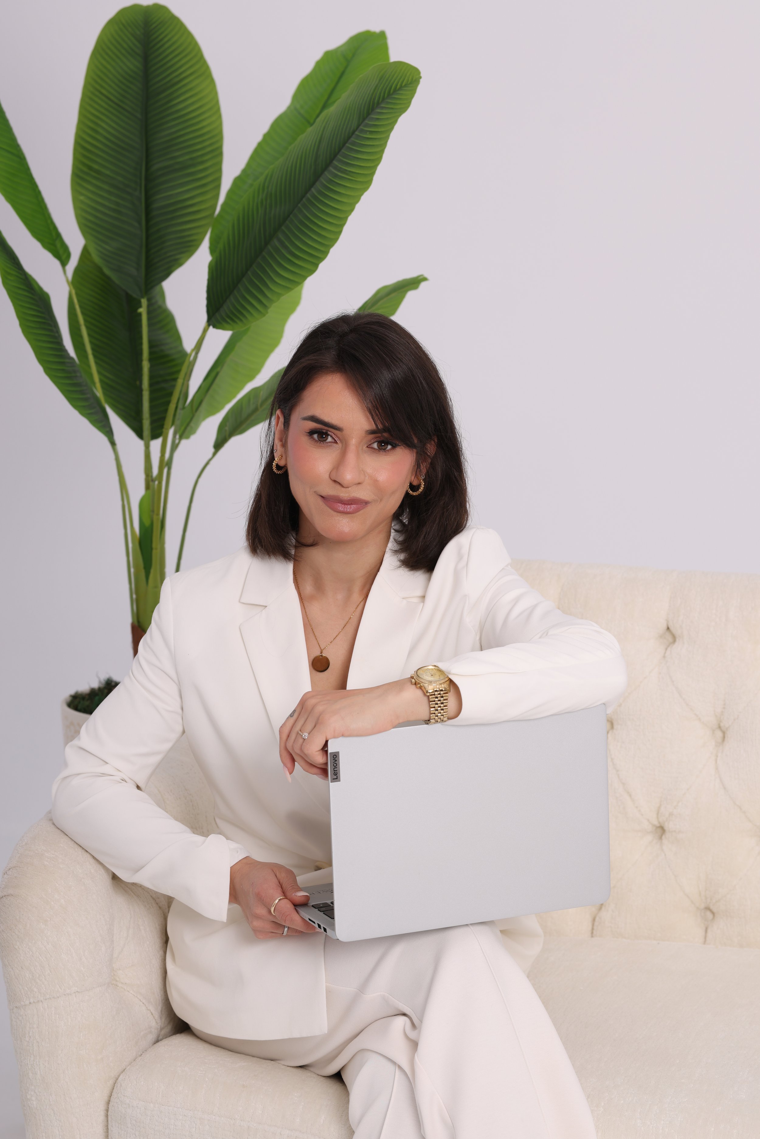 Marinela sitting on a sofa with a laptop, promoting holistic women’s wellness